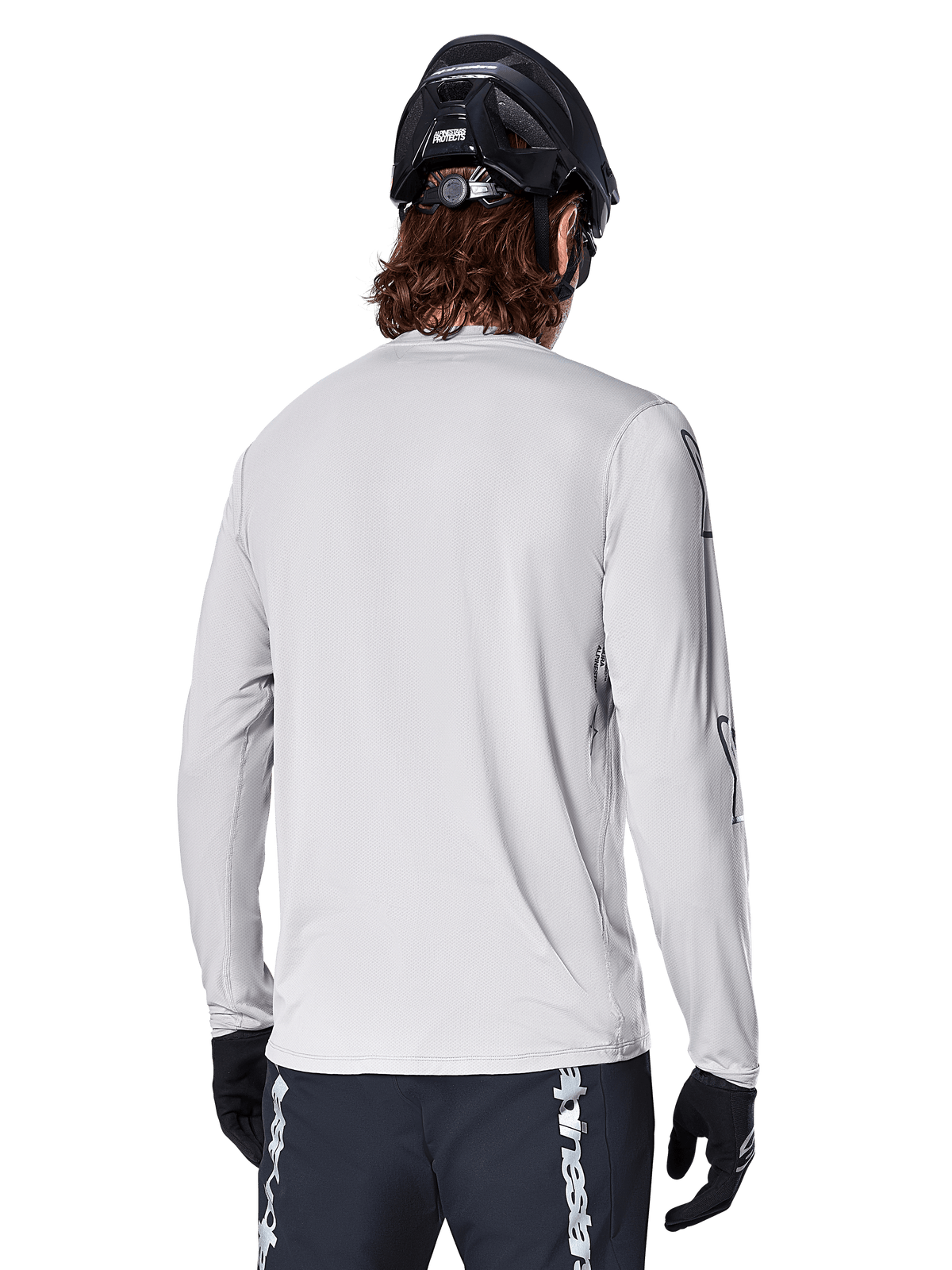 Alpinestars A-Dura Switch Langarmtrikot, Hellgrau, Rückansicht eines Mountainbikers mit schwarzem MTB-Helm und Handschuhen, mit verlängertem Rückensaum für zusätzliche Abdeckung und strukturiertem Jacquard-Gewebe, Performance-Radsportbekleidung.