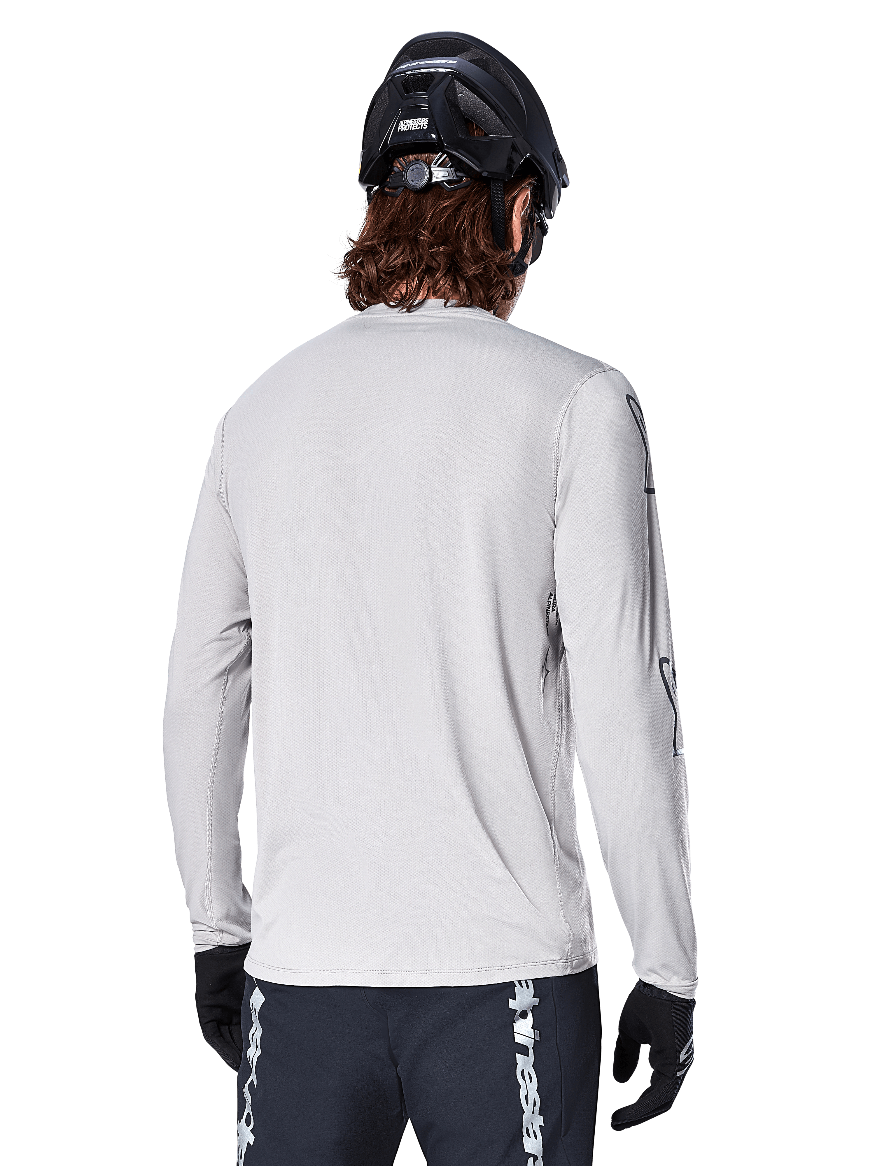 Alpinestars A-Dura Switch Langarmtrikot, Hellgrau, Rückansicht eines Mountainbikers mit schwarzem MTB-Helm und Handschuhen, mit verlängertem Rückensaum für zusätzliche Abdeckung und strukturiertem Jacquard-Gewebe, Performance-Radsportbekleidung.