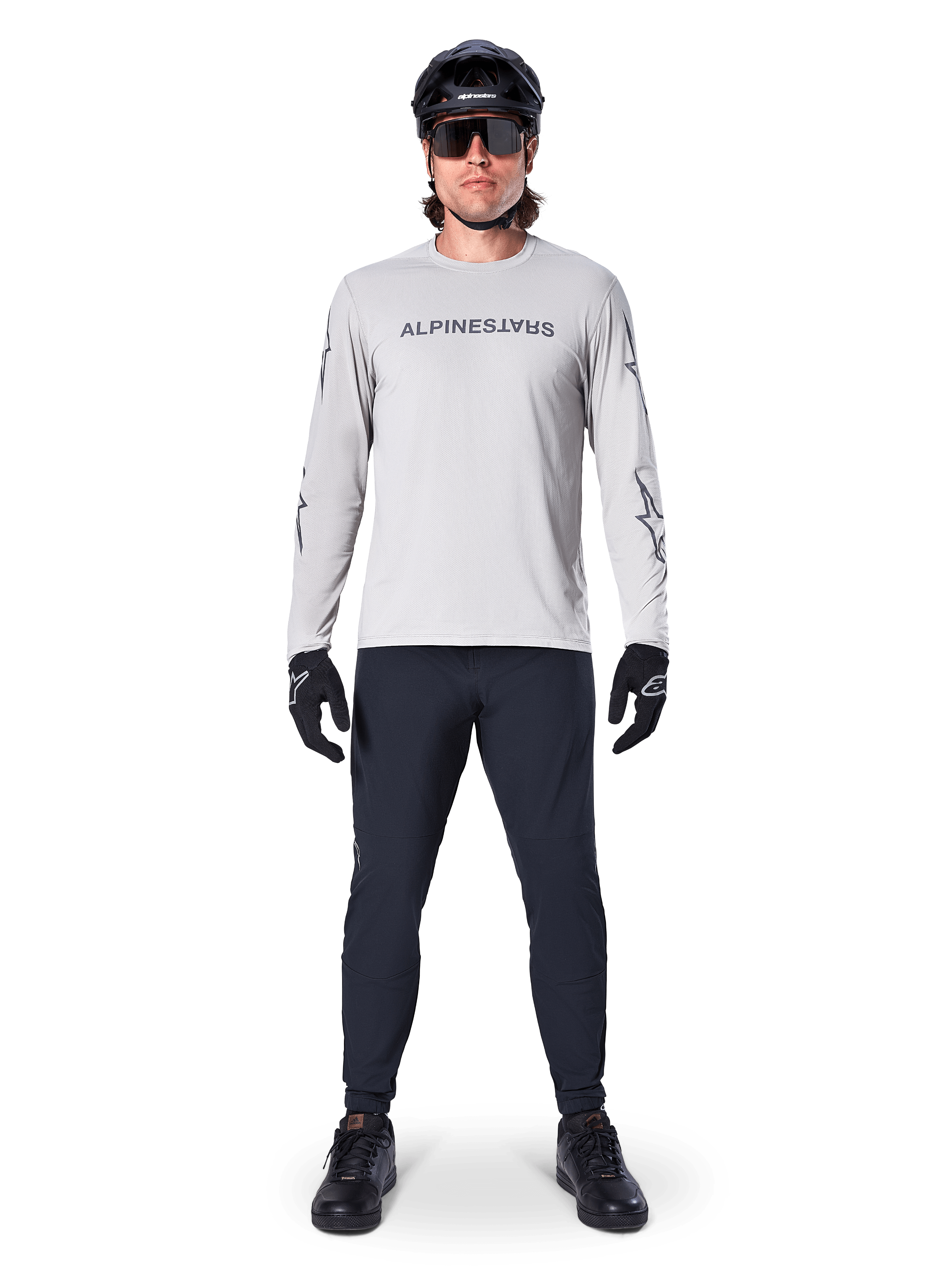 Alpinestars A-Dura Switch Langarmtrikot in Hellgrau, mit stilisiertem Wortmarken-Logo auf der Brust, getragen mit schwarzer Hose, Helm und Handschuhen, Performance-Mountainbike-Bekleidung für das Geländeradfahren