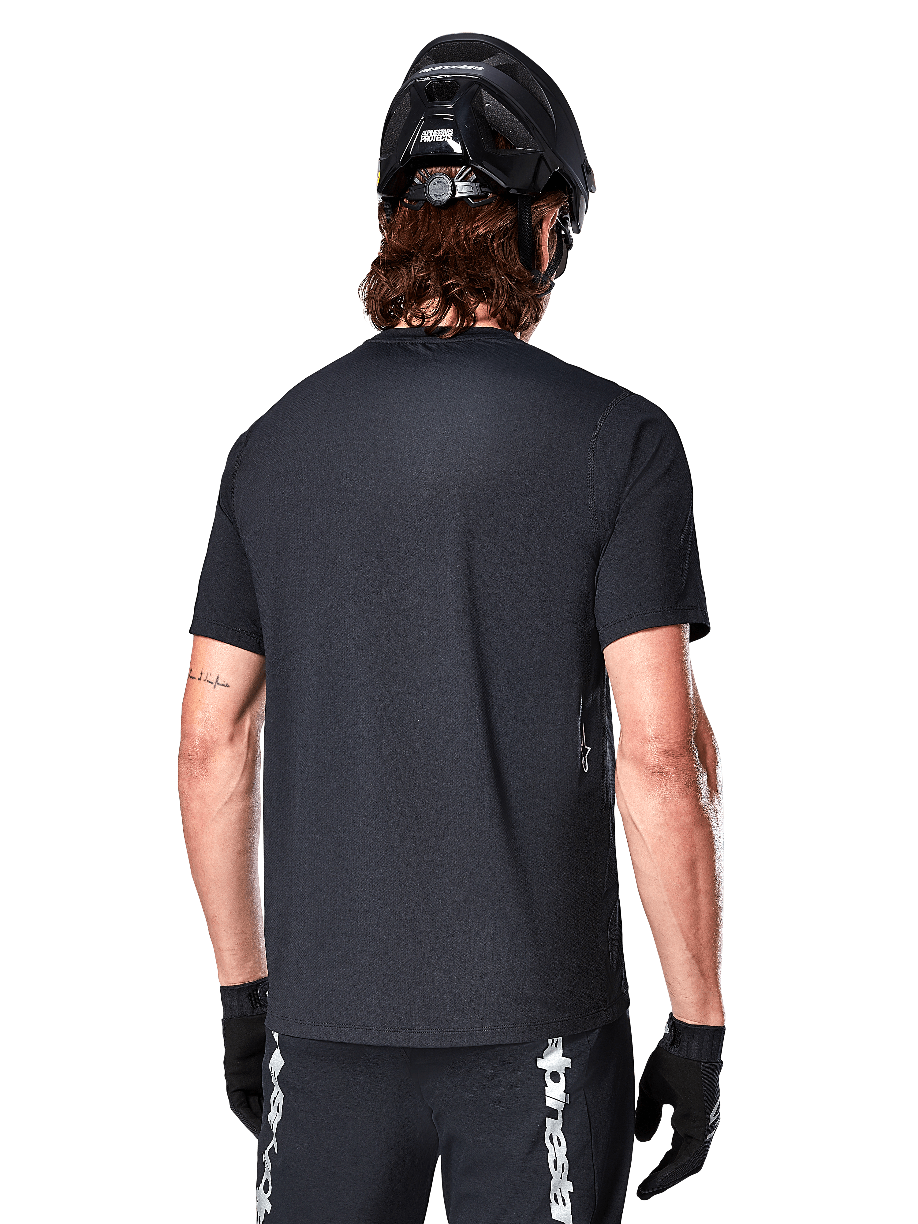 Alpinestars A-Dura Switch Kurzarmtrikot, Schwarz, Rückansicht eines Models mit schwarzem Fahrradhelm und MTB-Shorts, hebt die reguläre Passform und den verlängerten Rücken für das Mountainbiken hervor.