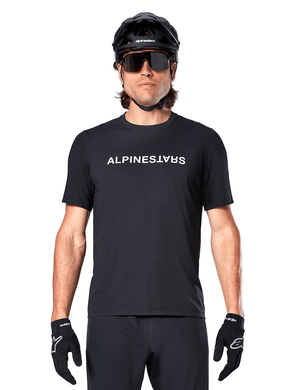 Mountainbike-Fahrer im Alpinestars A-Dura Switch Kurzarmtrikot in Schwarz, mit weißem Wortmarken-Logo auf der Brust, kombiniert mit schwarzem Helm, großer Sonnenbrille und schwarzen Handschuhen, professionelle Radsportbekleidung für Trail-Fahrten.