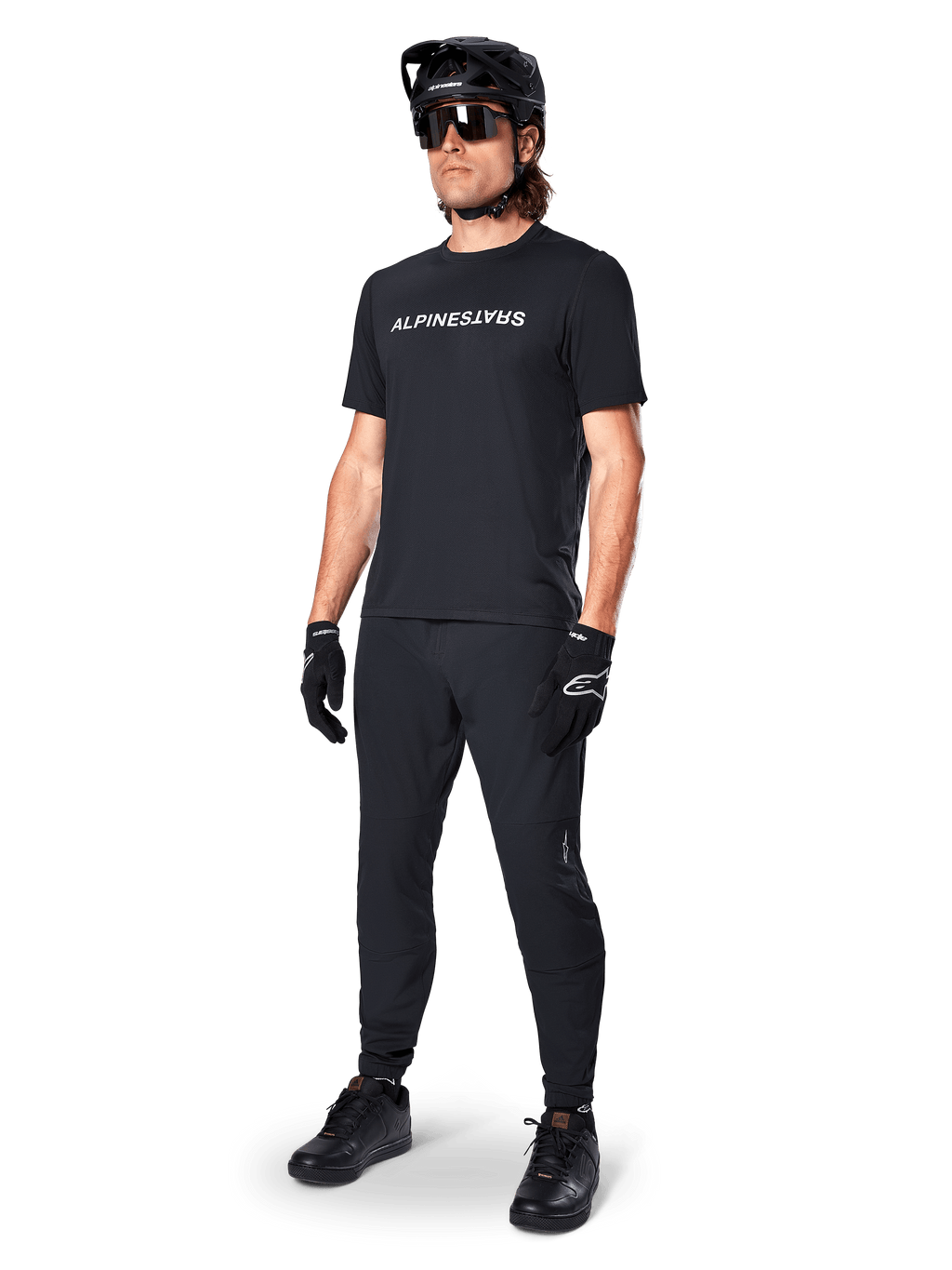 Alpinestars A-Dura Switch Kurzarmtrikot, Schwarz, getragen von einem Model mit passender schwarzer MTB-Hose, Helm und Handschuhen, mit weißer Alpinestars-Wortmarke auf der Brust, Performance-Mountainbike-Bekleidung