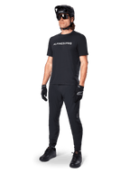 Alpinestars A-Dura Switch Kurzarmtrikot, Schwarz, getragen von einem Model mit passender schwarzer MTB-Hose, Helm und Handschuhen, mit weißer Alpinestars-Wortmarke auf der Brust, Performance-Mountainbike-Bekleidung