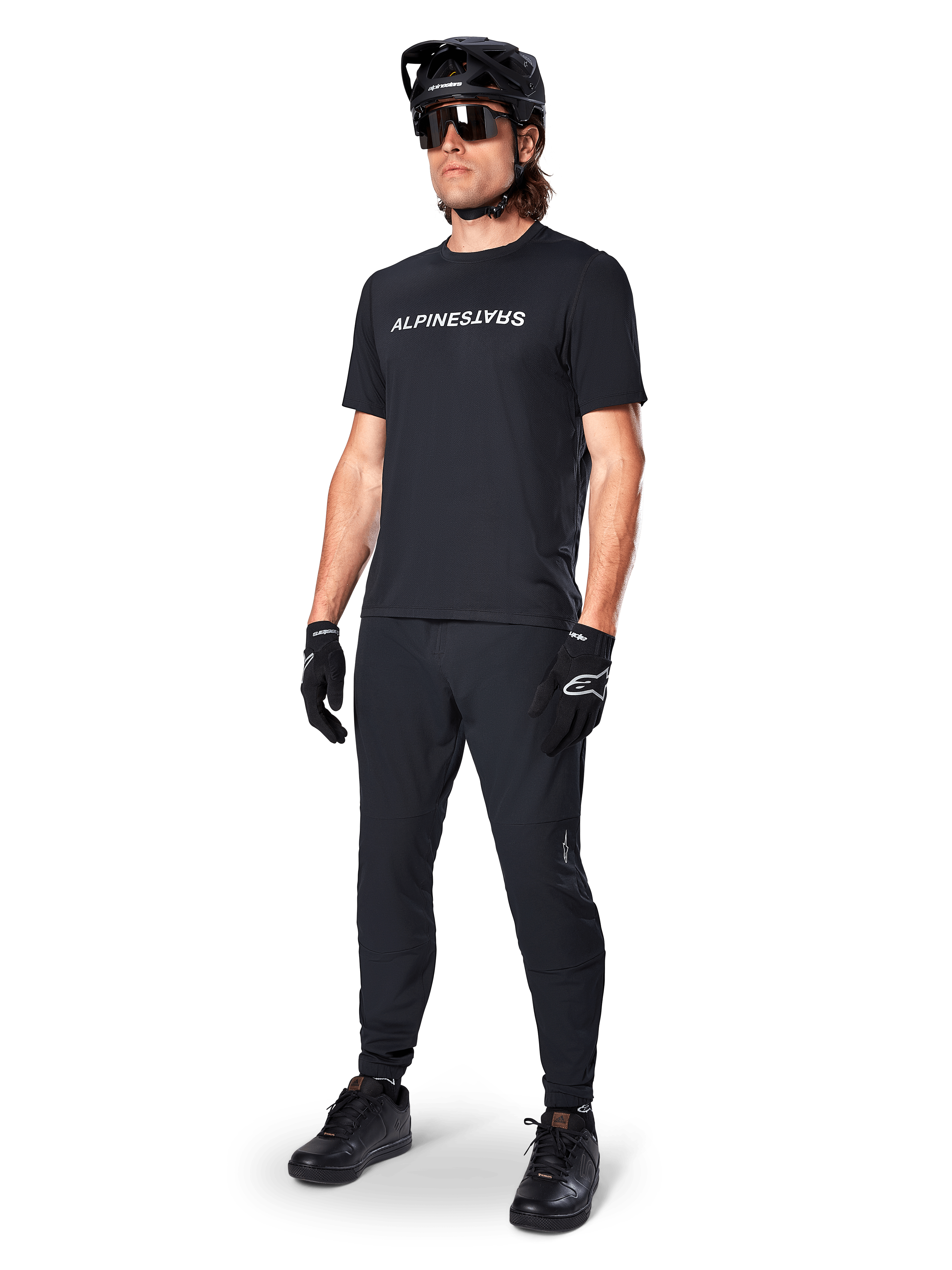 Alpinestars A-Dura Switch Kurzarmtrikot, Schwarz, getragen von einem Model mit passender schwarzer MTB-Hose, Helm und Handschuhen, mit weißer Alpinestars-Wortmarke auf der Brust, Performance-Mountainbike-Bekleidung