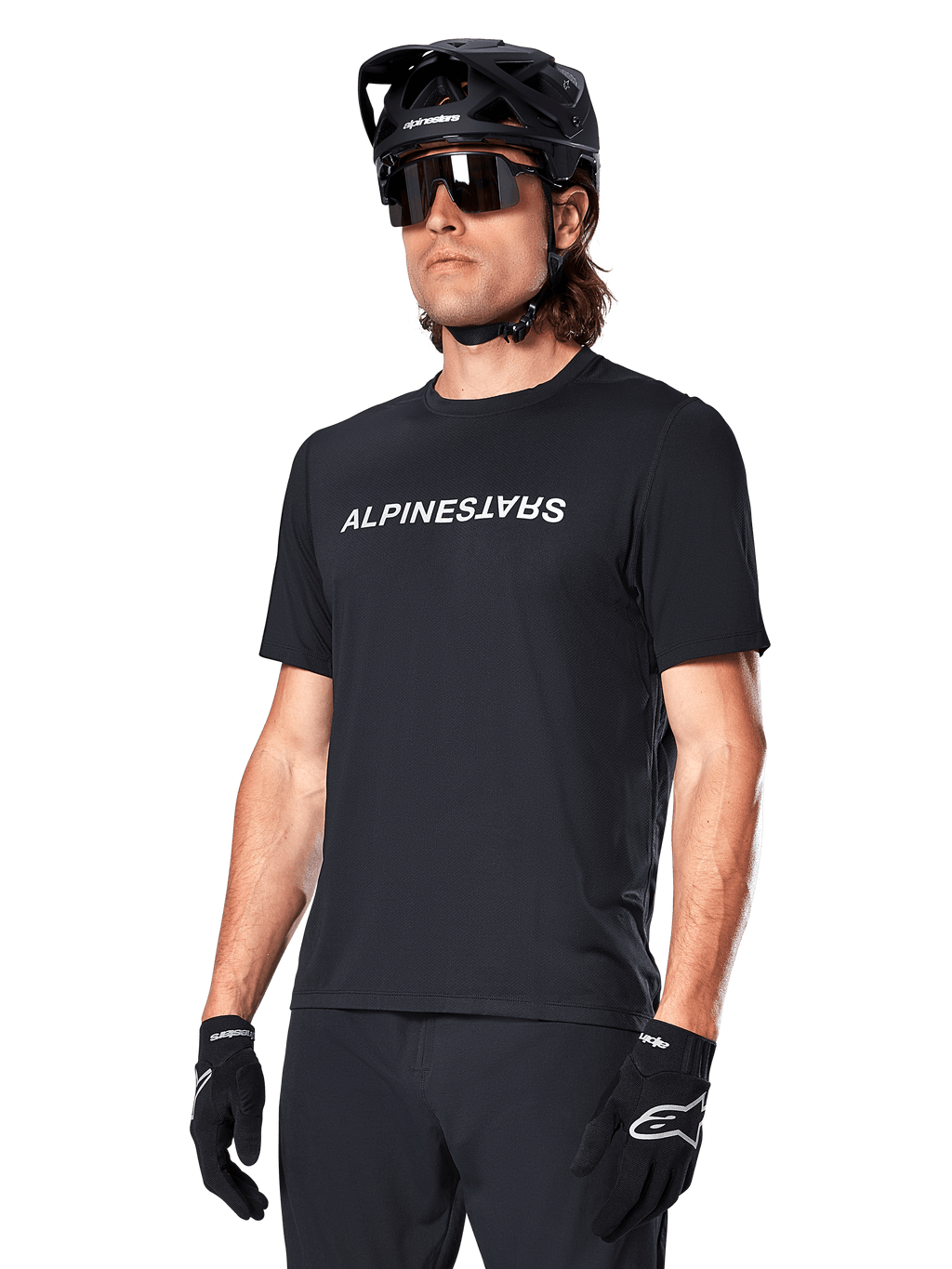 Alpinestars A-Dura Switch Kurzarmtrikot, Schwarz, mit weißem Wortmarken-Logo auf der Brust, getragen von einem Radfahrer mit schwarzem MTB-Helm und Sonnenbrille, technische Bekleidung für Trailriding