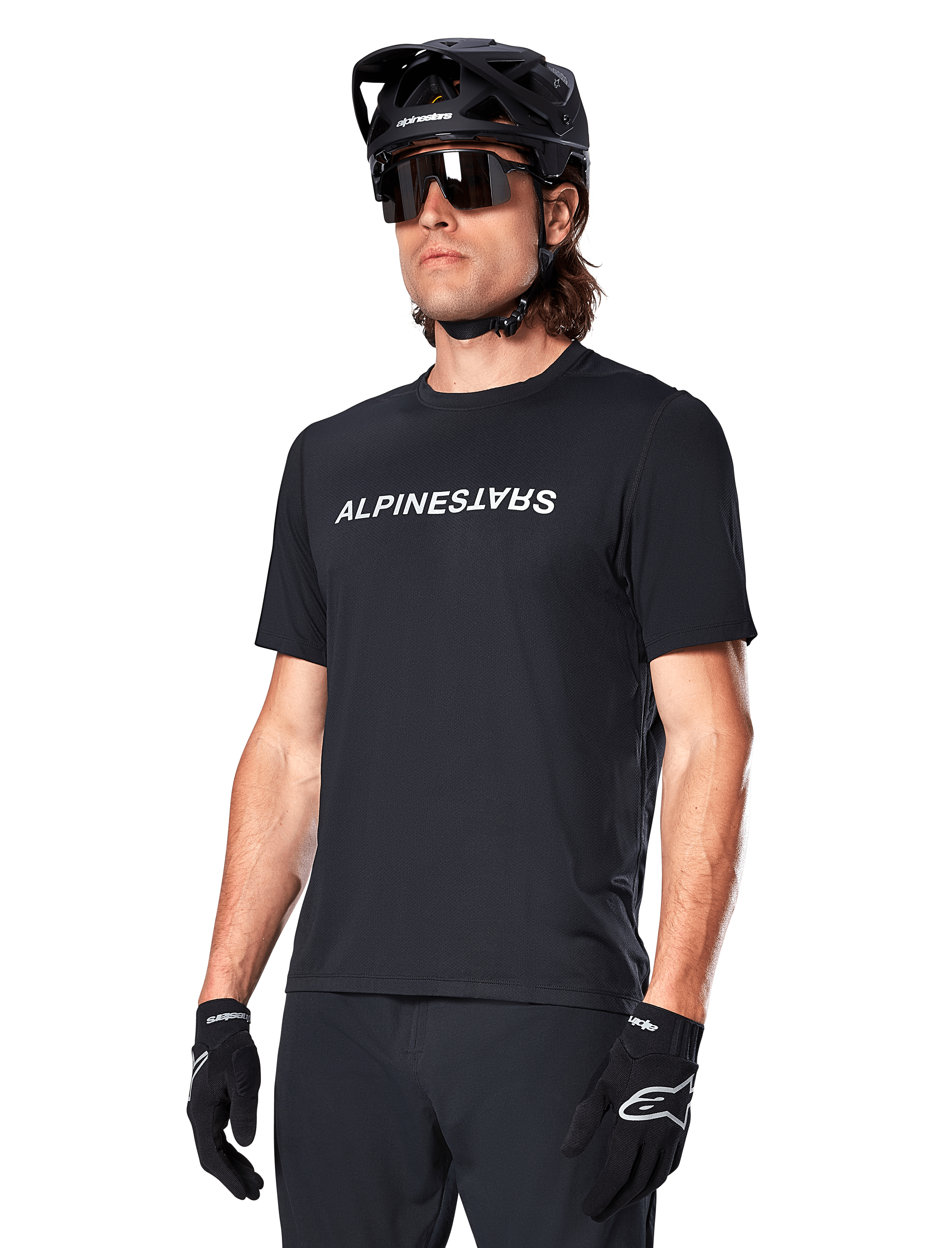 Alpinestars A-Dura Switch Kurzarmtrikot, Schwarz, mit weißem Wortmarken-Logo auf der Brust, getragen von einem Radfahrer mit schwarzem MTB-Helm und Sonnenbrille, technische Bekleidung für Trailriding