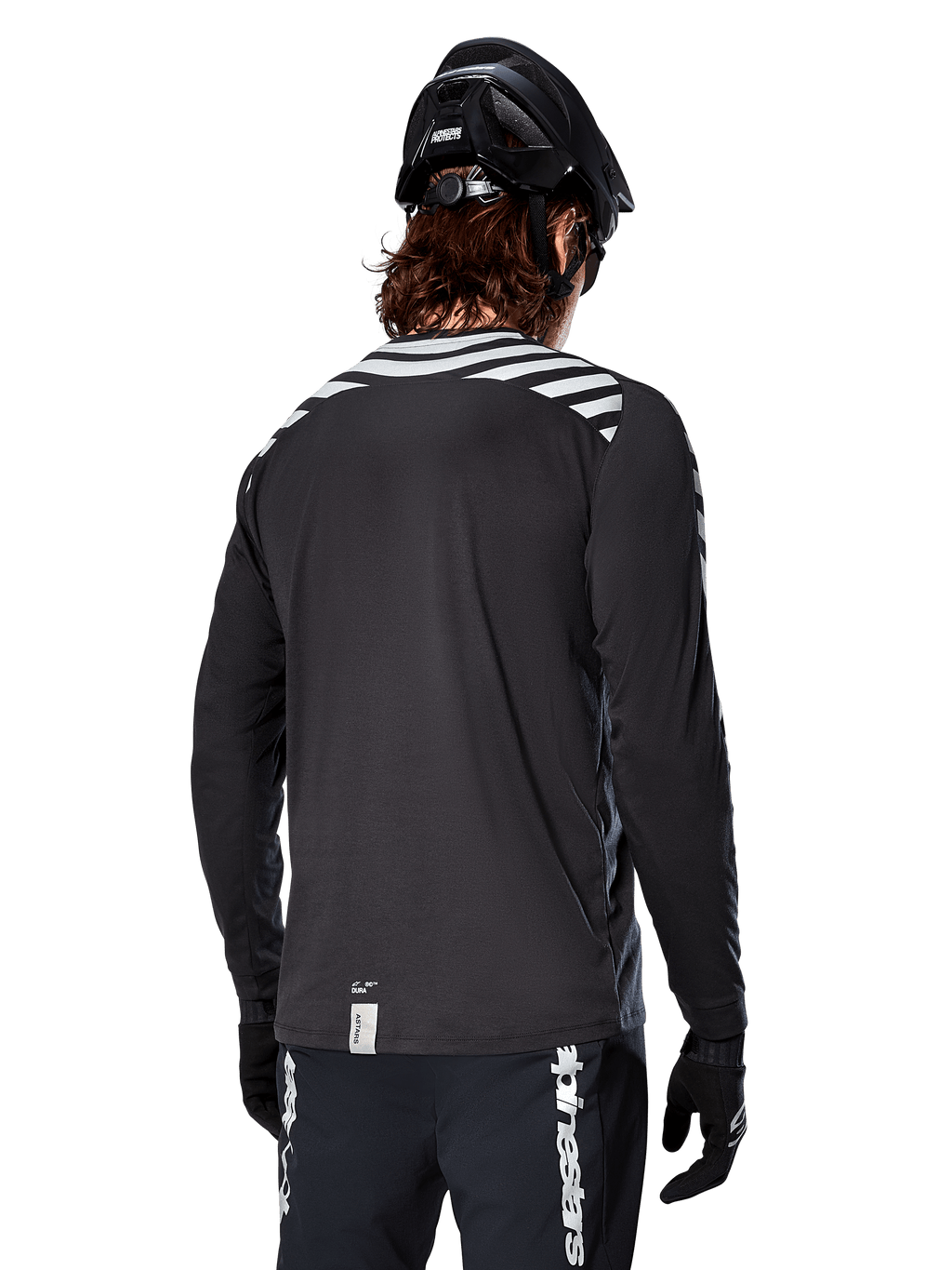 Alpinestars A-Dura Dri Oscar Long Sleeve Jersey, Black Reflective, rear view showing reflective diagonal stripes on shoulders and a longer drop tail, worn with black MTB helmet and gloves, technical gear for mountain biking