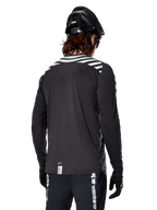 Alpinestars A-Dura Dri Oscar Long Sleeve Jersey, Black Reflective, rear view showing reflective diagonal stripes on shoulders and a longer drop tail, worn with black MTB helmet and gloves, technical gear for mountain biking