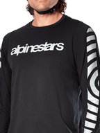 Alpinestars A-Dura Dri Oscar Long Sleeve Jersey, Black Reflective, close-up view showing white alpinestars logo on the chest and reflective circular graphics on the sleeves, technical cycling apparel for mountain biking