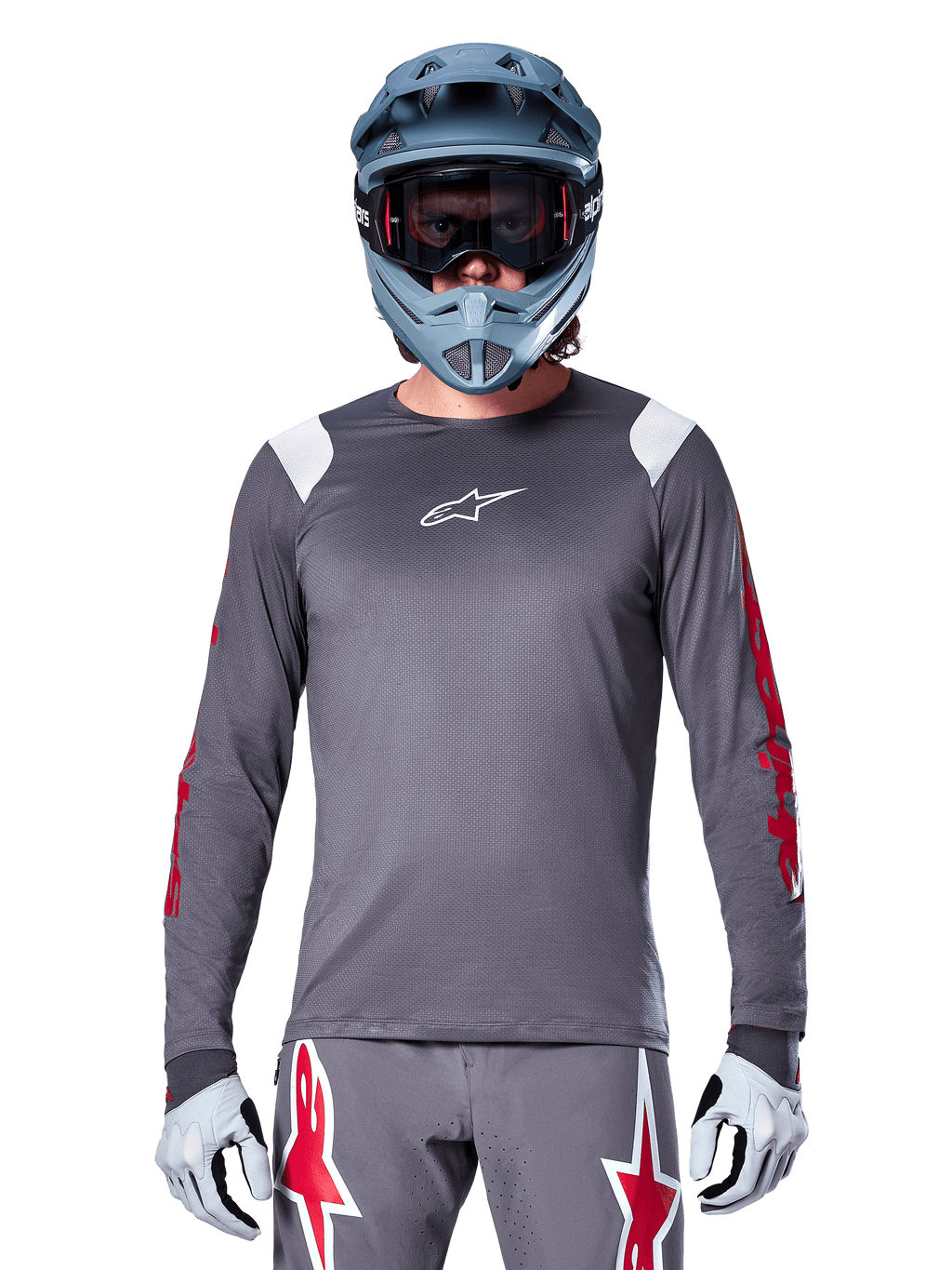 MTB-Fahrer im Alpinestars A-Supra Astar Langarmtrikot, Dunkelgrau mit roten Grafiken an den Ärmeln und weißen Schulterakzenten, passender grauer Hose mit roten Stern-Logos, blauem Fullface-Helm und Goggle, abgestimmte Offroad-Radsportausrüstung