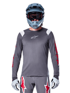 MTB-Fahrer im Alpinestars A-Supra Astar Langarmtrikot, Dunkelgrau mit roten Grafiken an den Ärmeln und weißen Schulterakzenten, passender grauer Hose mit roten Stern-Logos, blauem Fullface-Helm und Goggle, abgestimmte Offroad-Radsportausrüstung