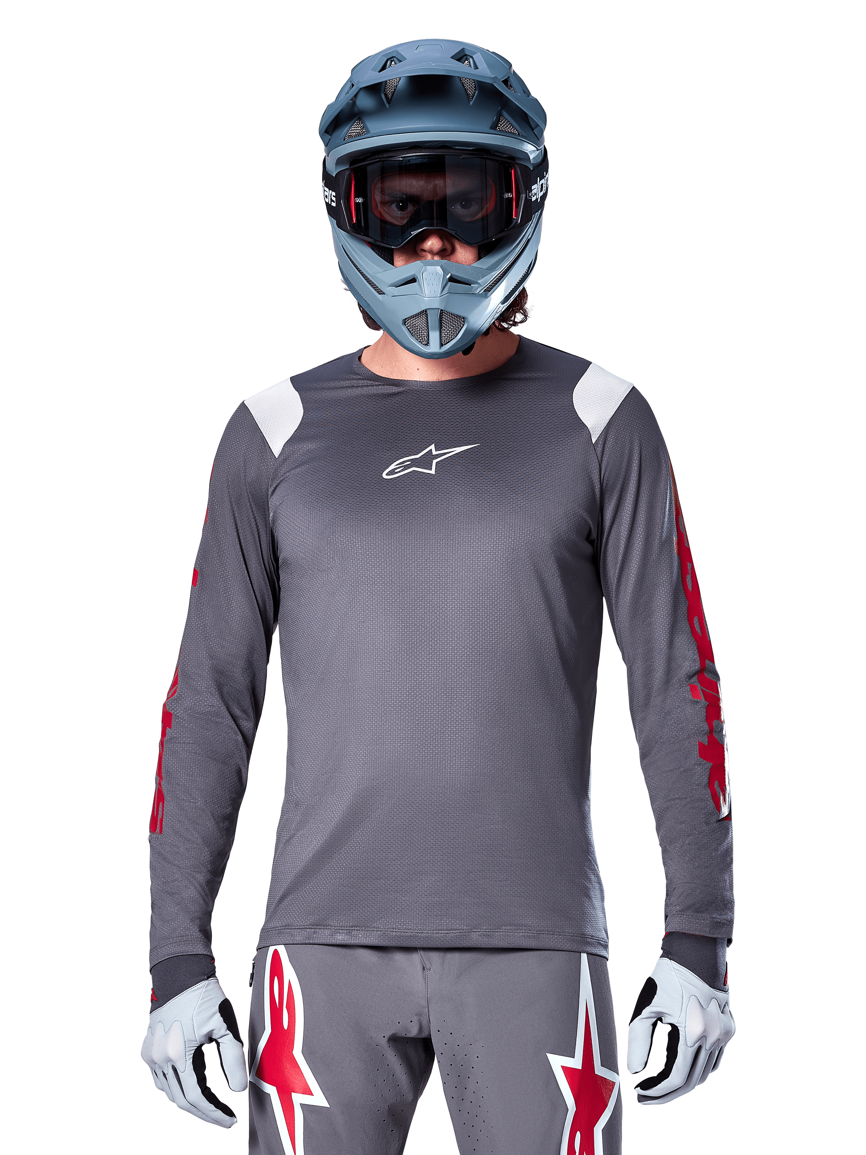 MTB-Fahrer im Alpinestars A-Supra Astar Langarmtrikot, Dunkelgrau mit roten Grafiken an den Ärmeln und weißen Schulterakzenten, passender grauer Hose mit roten Stern-Logos, blauem Fullface-Helm und Goggle, abgestimmte Offroad-Radsportausrüstung