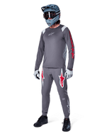 Alpinestars A-Supra Astar Langarmtrikot in Dunkelgrau, mit rotem Branding auf den Ärmeln und weißem Logo auf der Brust, getragen von einem Fahrer mit passender grauer Hose, einem blaugrauen Full-Face-Helm und Performance-Handschuhen, koordinierte Mountainbike-Ausrüstung für Gravity-Riding.