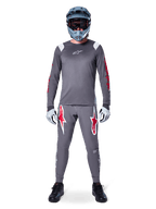 MTB-Fahrer im Alpinestars A-Supra Astar Langarmtrikot, Dunkelgrau mit roten Akzenten und weißem Brust-Logo, dazu passende graue Hose mit großen roten Sterngrafiken, blauer Fullface-Helm mit Goggle, hellgraue Handschuhe und schwarze Schuhe, professionelle Mountainbike-Ausrüstung