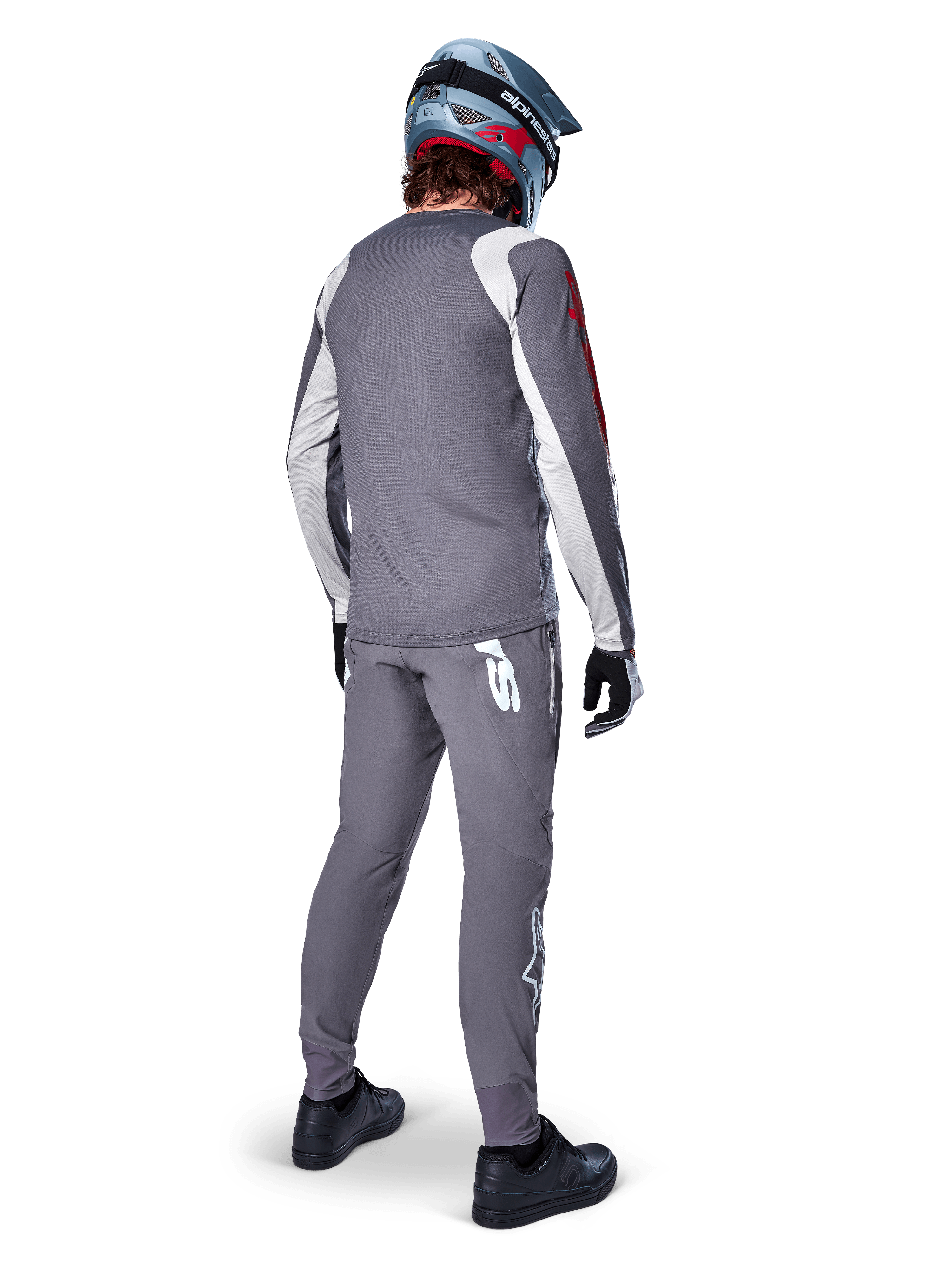 Alpinestars A-Supra Astar Trikot, Langarm-MTB-Trikot, Dunkelgrau mit weißen Ärmelakzenten und rotem Logo, Rückansicht eines Fahrers in passender grauer Hose und blauem Full-Face-Helm, Performance-Radsportbekleidung