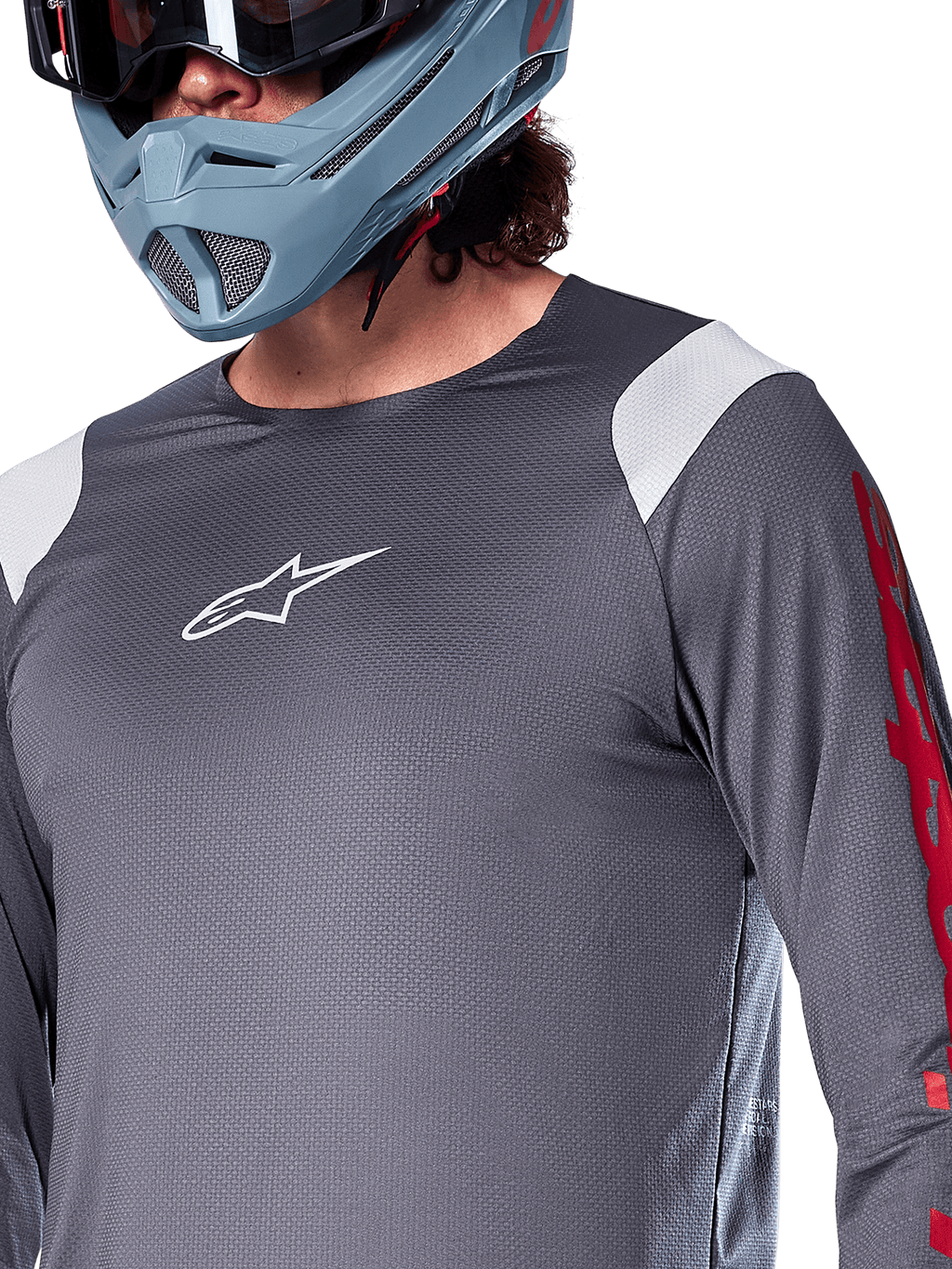 Alpinestars A-Supra Astar Langarmtrikot, Dunkelgrau mit weißen Schultereinsätzen und roten Grafiken am Ärmel, getragen mit einem hellblau-grauen Full-Face-Helm, Performance-Mountainbike-Bekleidung