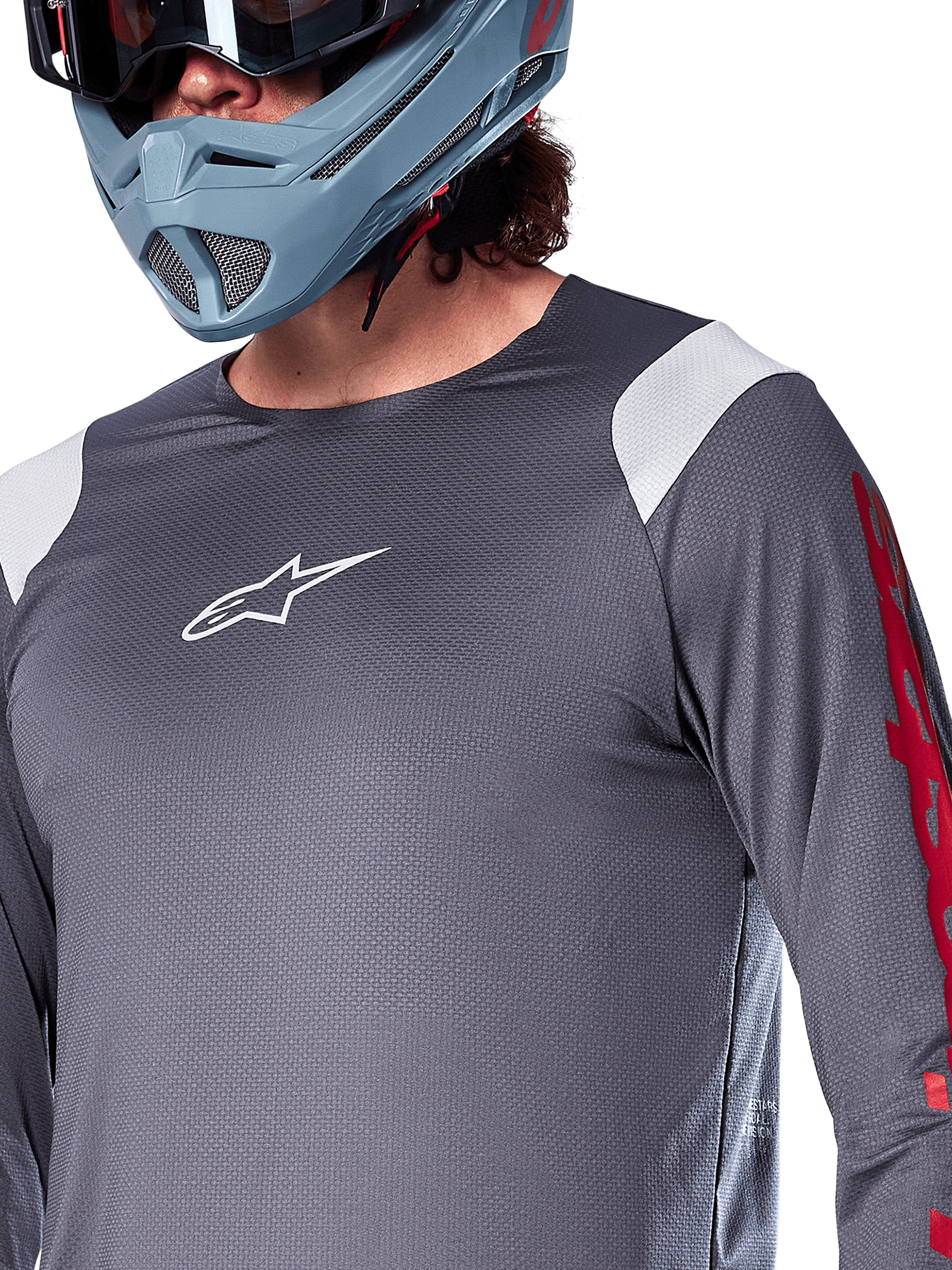 Alpinestars A-Supra Astar Langarmtrikot, Dunkelgrau mit weißen Schultereinsätzen und roten Grafiken am Ärmel, getragen mit einem hellblau-grauen Full-Face-Helm, Performance-Mountainbike-Bekleidung