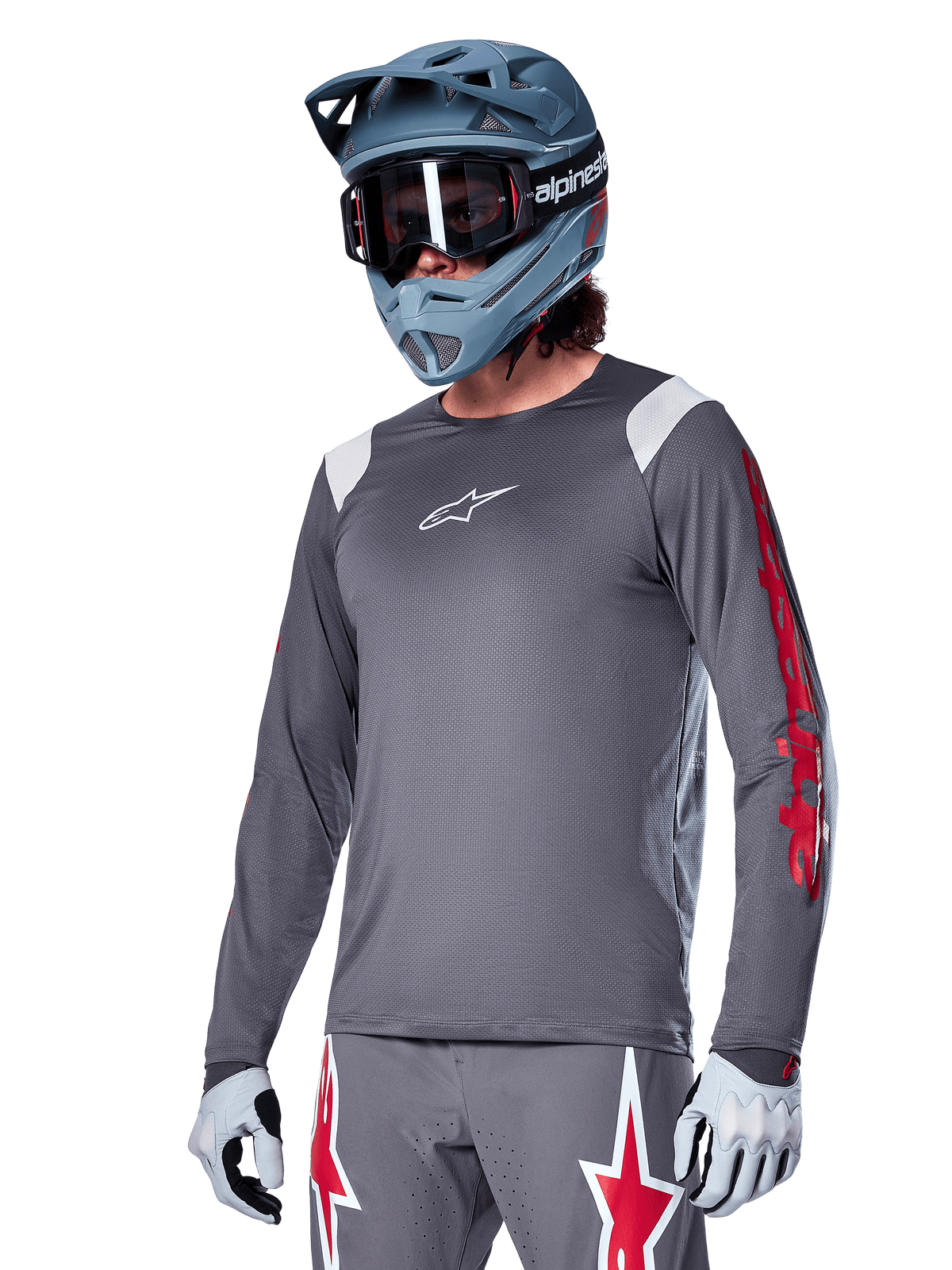 Alpinestars A-Supra Astar Langarmtrikot, MTB-Trikot, Dunkelgrau mit roten und weißen Akzenten, Performance-Passform, getragen mit passender grauer Hose mit roten und weißen Sterngrafiken, komplettes Offroad-Cycling-Outfit mit Full-Face-Helm und Handschuhen