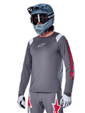 Alpinestars A-Supra Astar Langarmtrikot, MTB-Trikot, Dunkelgrau mit roten und weißen Akzenten, Performance-Passform, getragen mit passender grauer Hose mit roten und weißen Sterngrafiken, komplettes Offroad-Cycling-Outfit mit Full-Face-Helm und Handschuhen