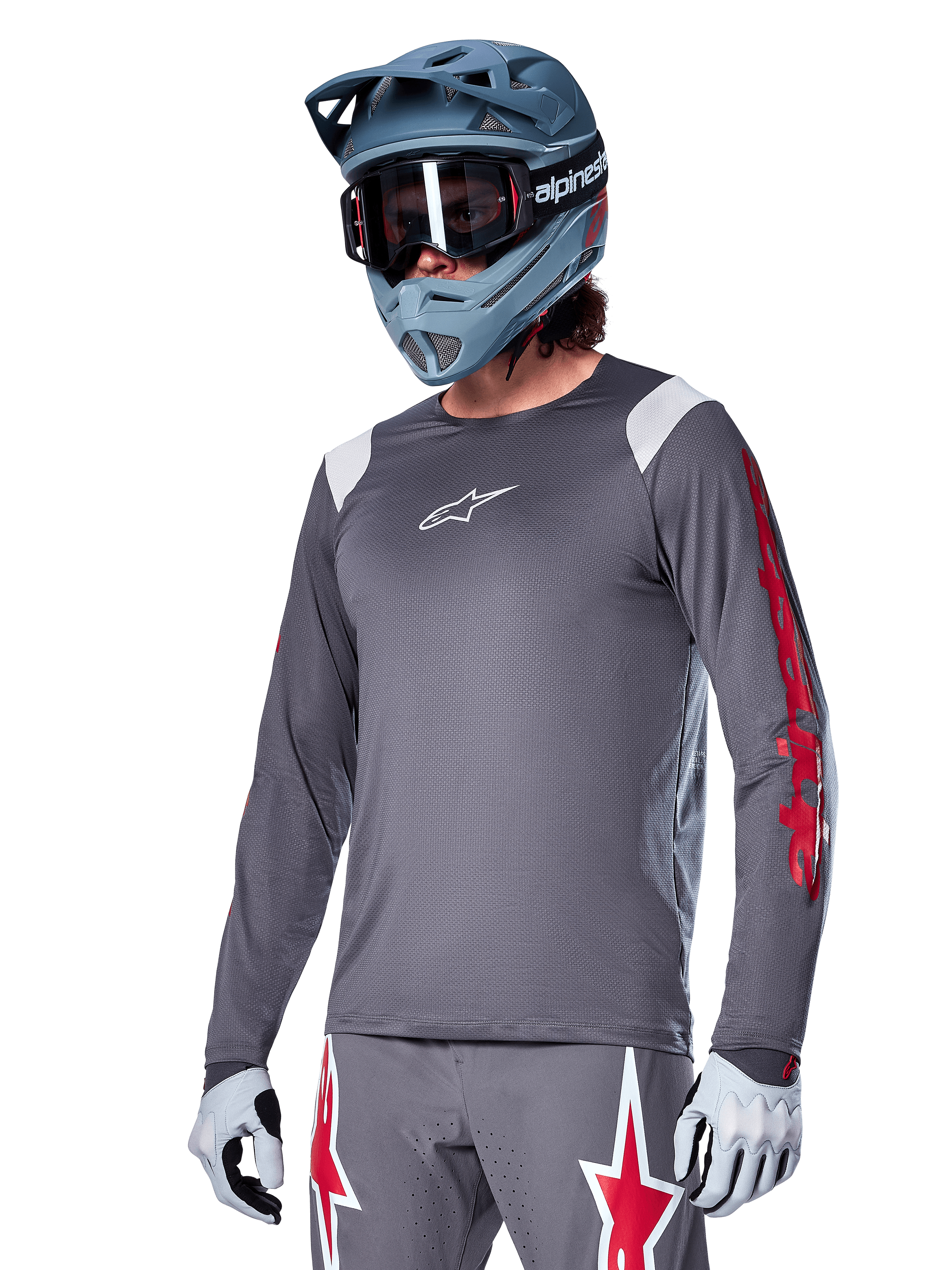 Alpinestars A-Supra Astar Langarmtrikot, MTB-Trikot, Dunkelgrau mit roten und weißen Akzenten, Performance-Passform, getragen mit passender grauer Hose mit roten und weißen Sterngrafiken, komplettes Offroad-Cycling-Outfit mit Full-Face-Helm und Handschuhen