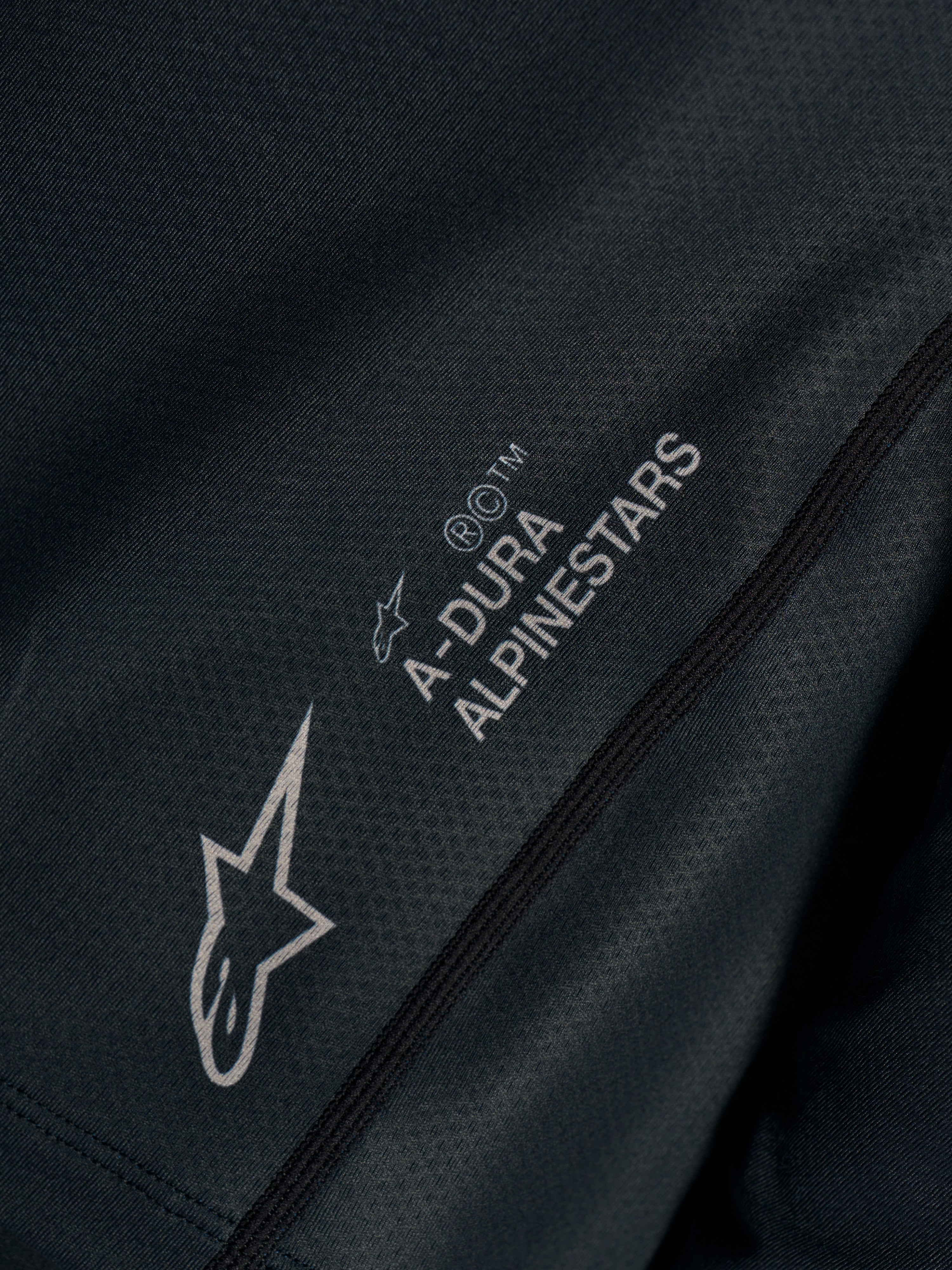 Schwarzes Stella A-Dura Ride Trikot in Nahaufnahme, technisches Jacquard-Gewebe mit A-DURA ALPINESTARS und Astars-Logos.
