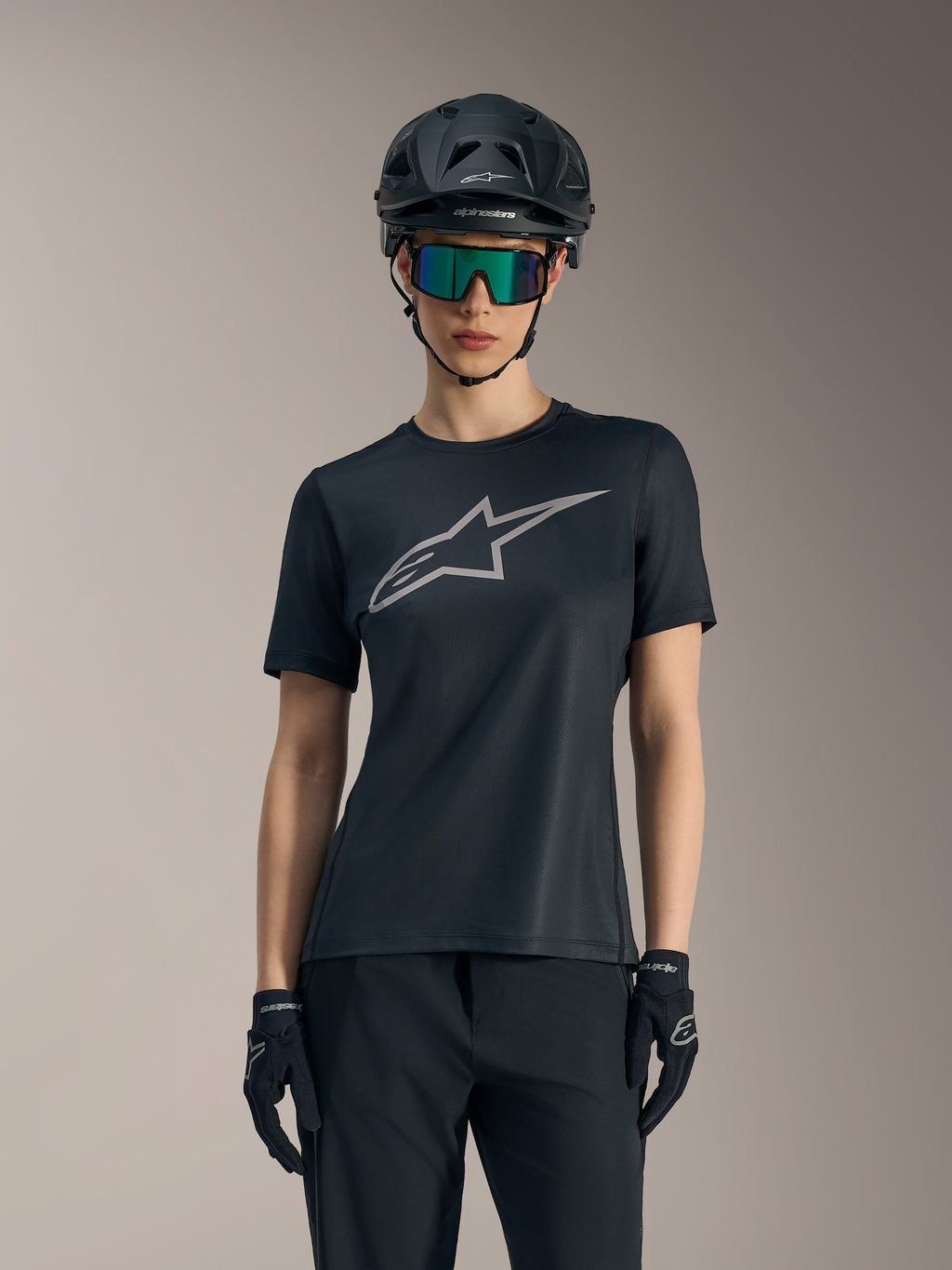 Schwarzes Stella A-Dura Ride Damen-Trikot mit grauem Brustlogo, kombiniert mit MTB-Helm, Goggles und Handschuhen.