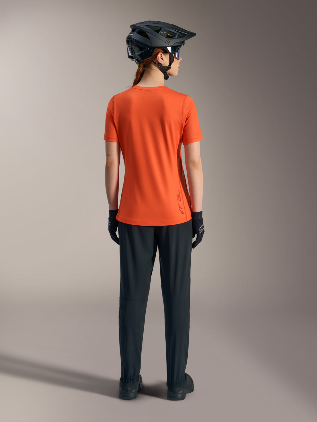 Alpinestars Stella A-Dura Ride Kurzarmtrikot für Damen in Orange, Rückansicht mit schwarzer MTB-Hose und Helm.