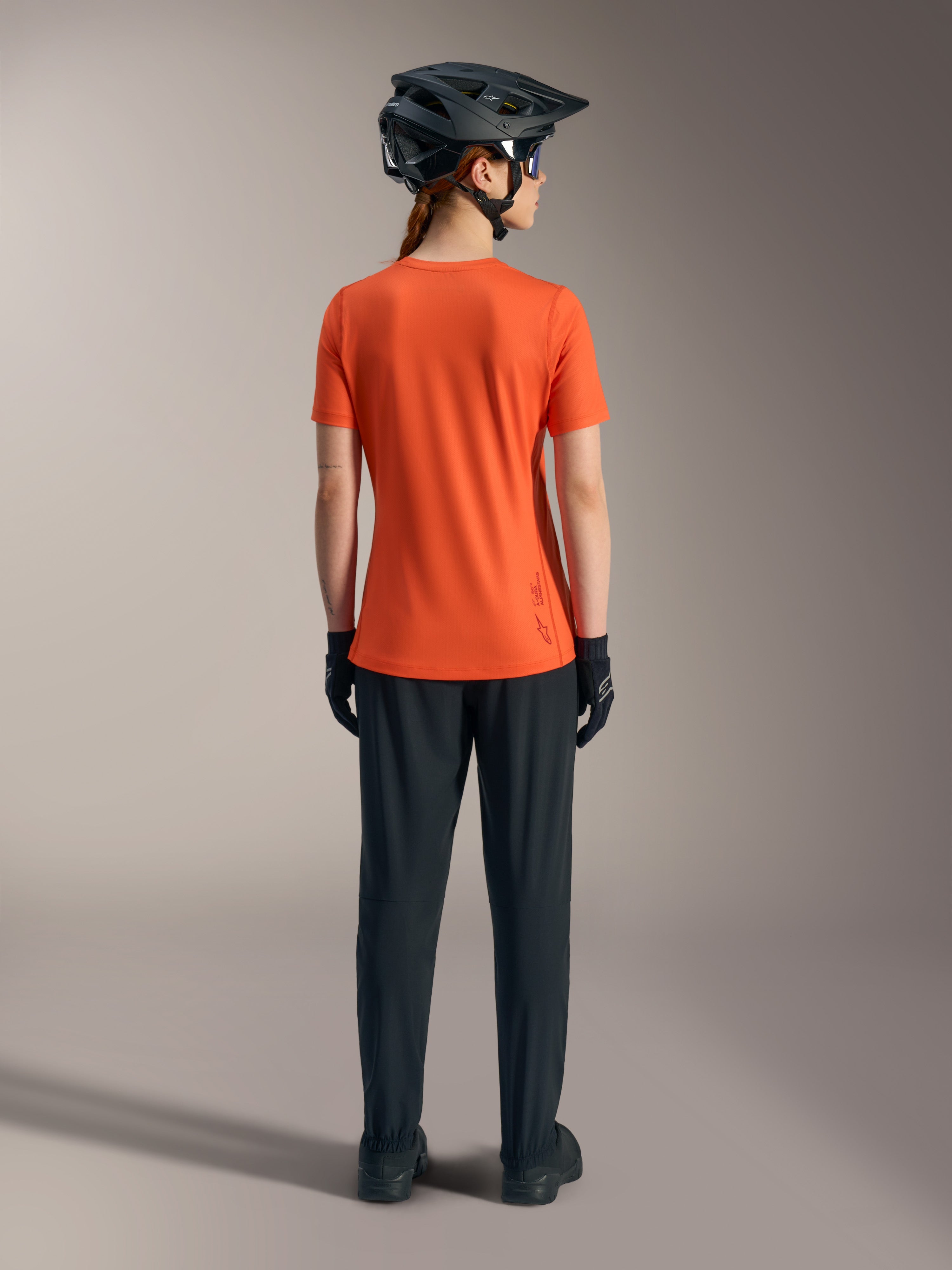Alpinestars Stella A-Dura Ride Kurzarmtrikot für Damen in Orange, Rückansicht mit schwarzer MTB-Hose und Helm.