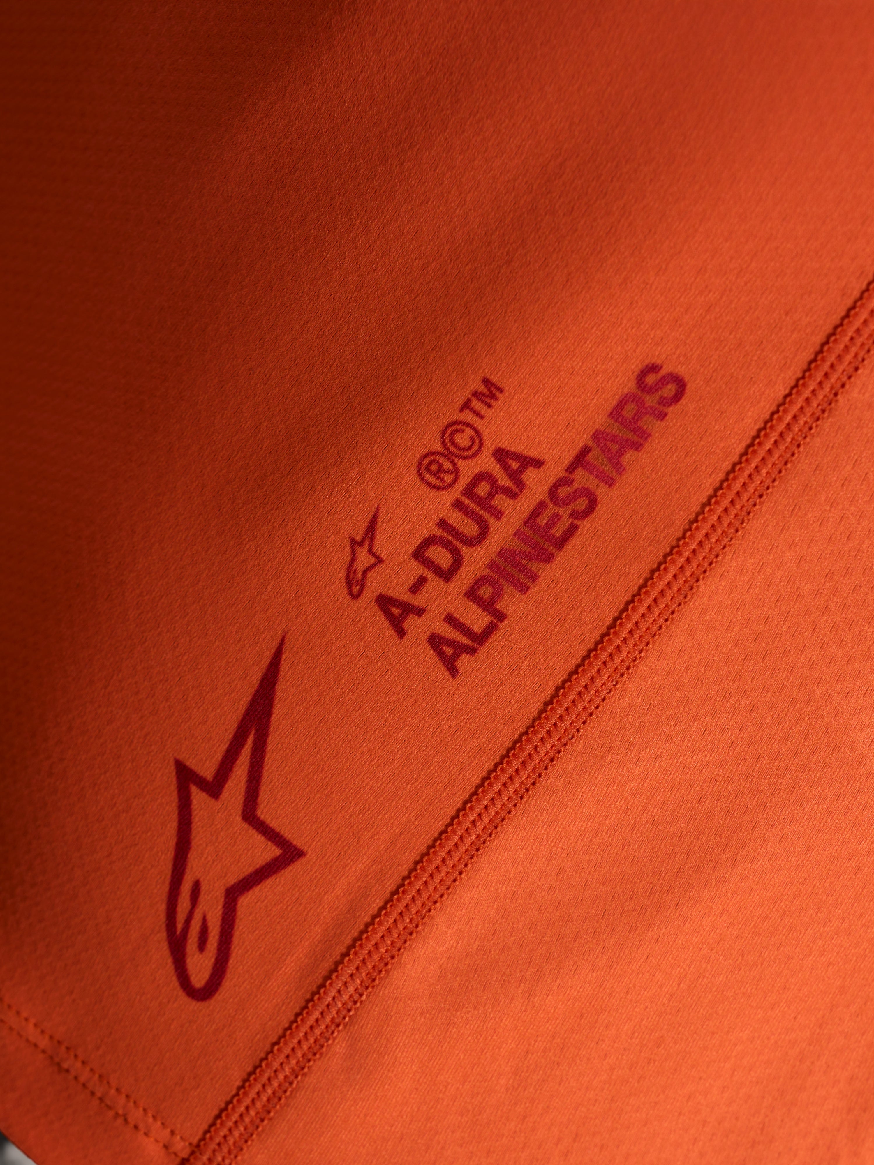 Oranges Stella A-Dura Ride Trikot-Detail mit Alpinestars Logo und A-DURA Schriftzug auf technischem Stretchgewebe.