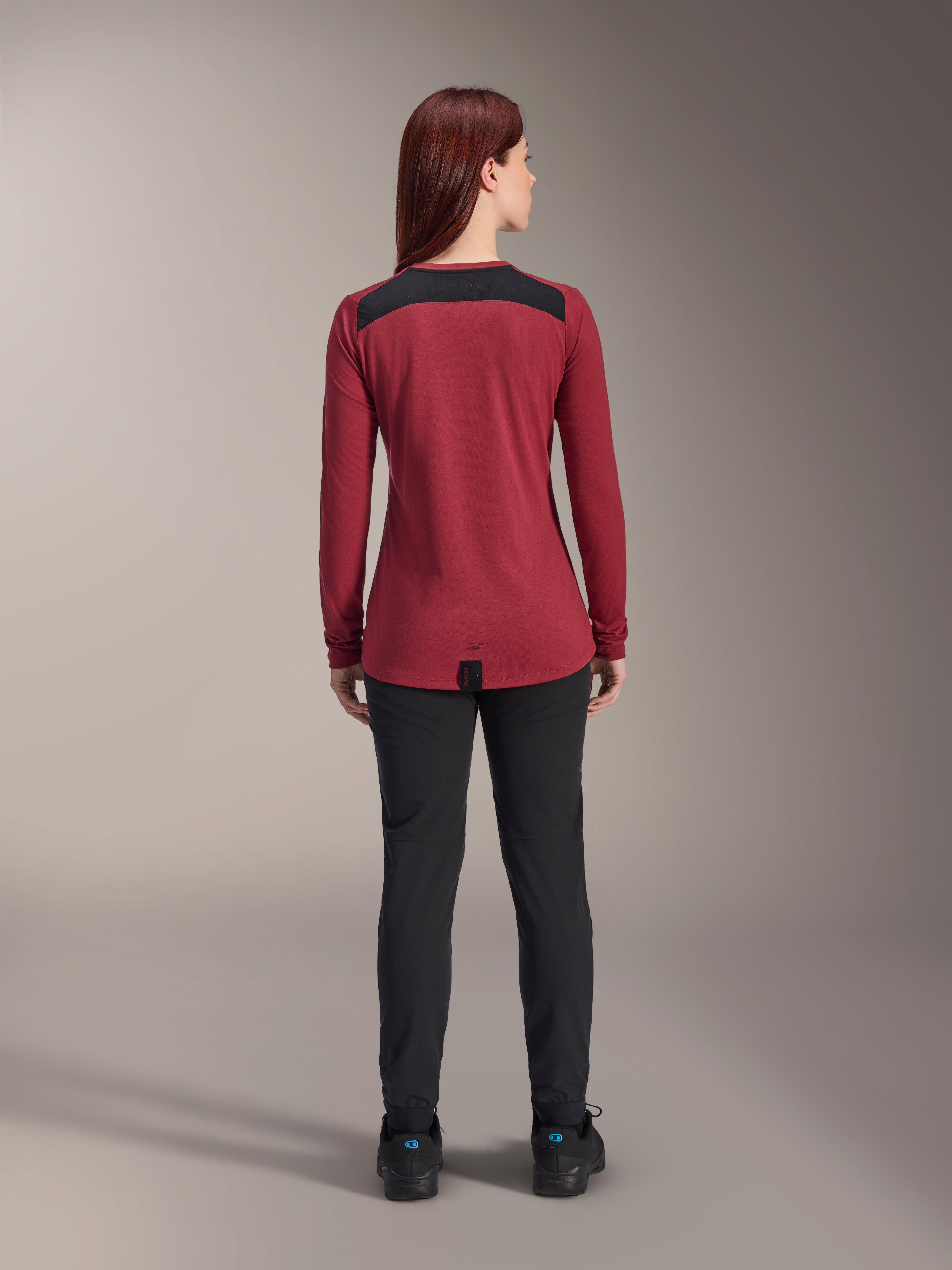 Alpinestars Women Stella A-Dura Dri Astar Long Sleeve Jersey, Burgundy Red with black mesh shoulder panels, technical MTB apparel shown from the back with black pants, drop tail design for cycling coverage