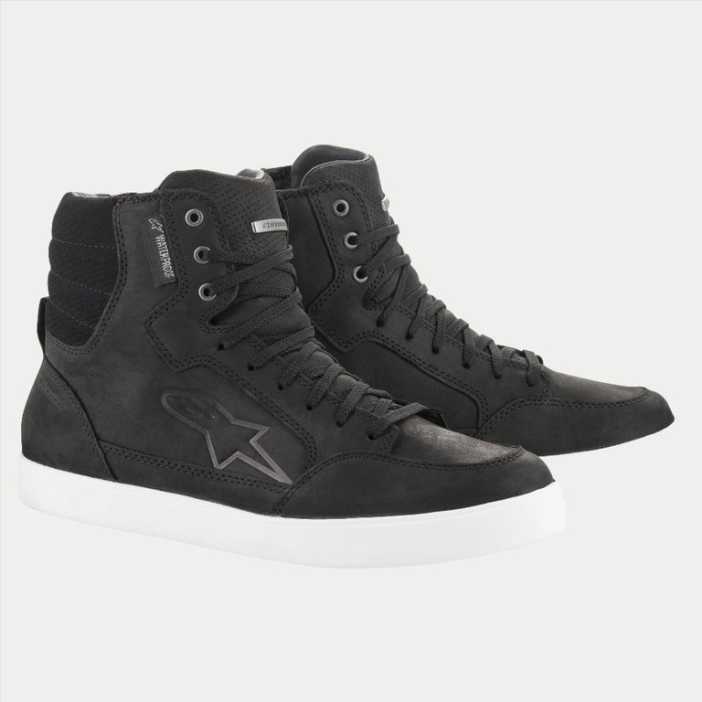 The J-6 Waterproof Shoe by Alpinestars EU is a pair of black high-top sneakers with white soles, made from high-quality leather. These shoes feature a star logo on the side, padded ankles, and lace-up closures. The background is plain white.