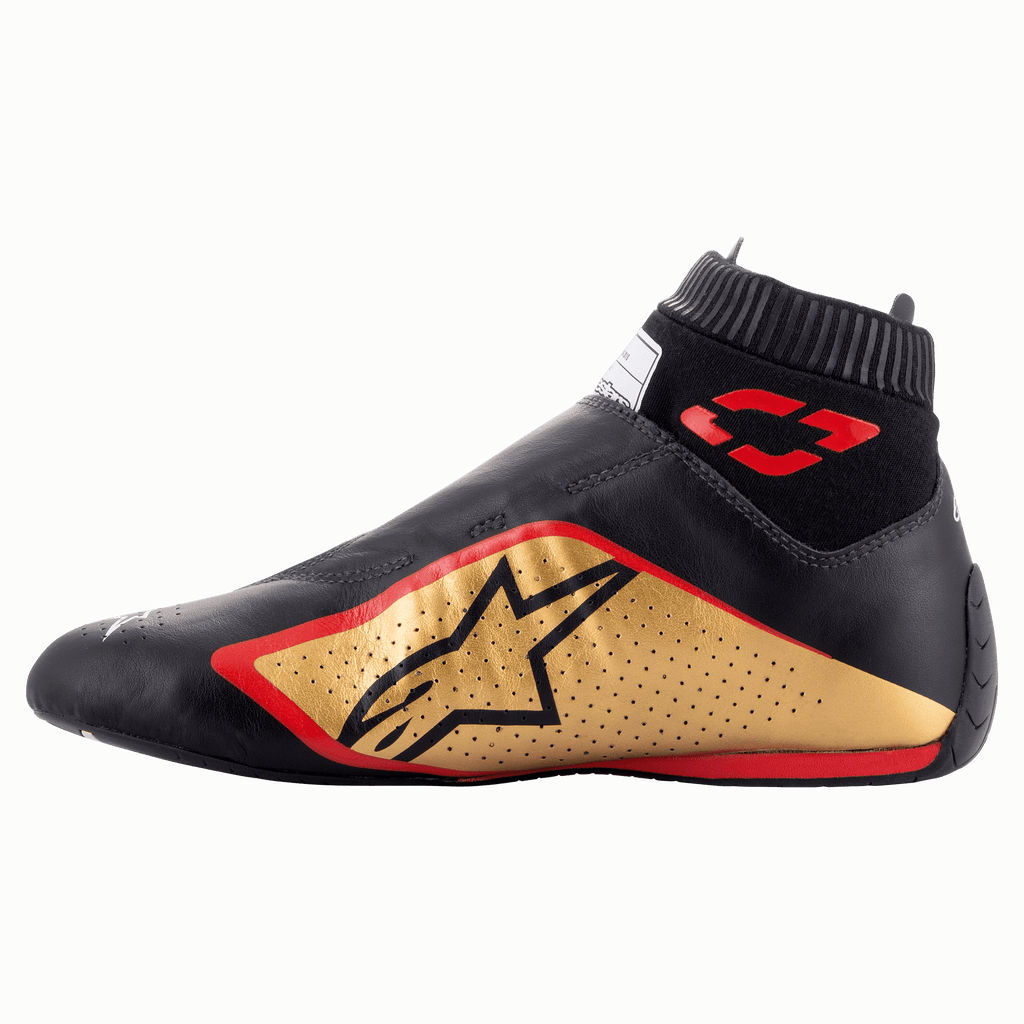 Alpinestars Supermono V2 Schuhe FIA, Auto-Rennschuhe, Schwarz, Gold und Rot, Seitenprofilansicht mit einer eleganten, einteiligen Lederkonstruktion, goldenem Seitenpanel mit schwarzem Stern-Logo, roten Akzenten und einem gerippten elastischen Kragen.