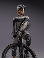 Graues Alpinestars A-Dura Race Langarmtrikot an einem MTB-Fahrer, mit schwarzen Akzenten und Profi-Radausrüstung.