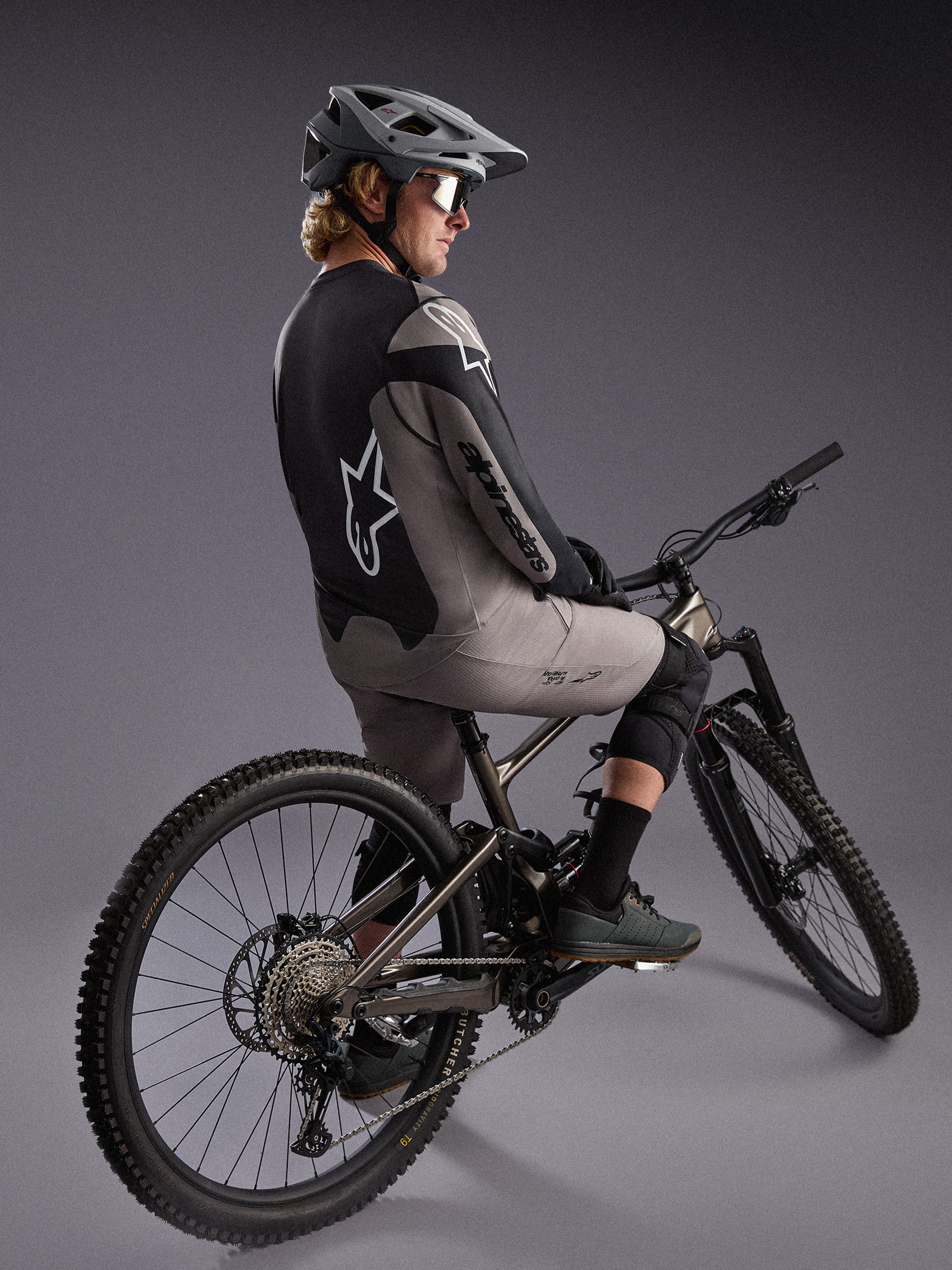 Graues A-Dura Race Langarmtrikot an einem Mountainbiker, mit markanten Alpinestars-Logos und Performance-Stretchgewebe.