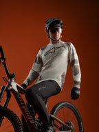 A-Dura Ride Langarmtrikot in Sand Camo mit Alpinestars-Logo, getragen von einem MTB-Fahrer auf einem Mountainbike.