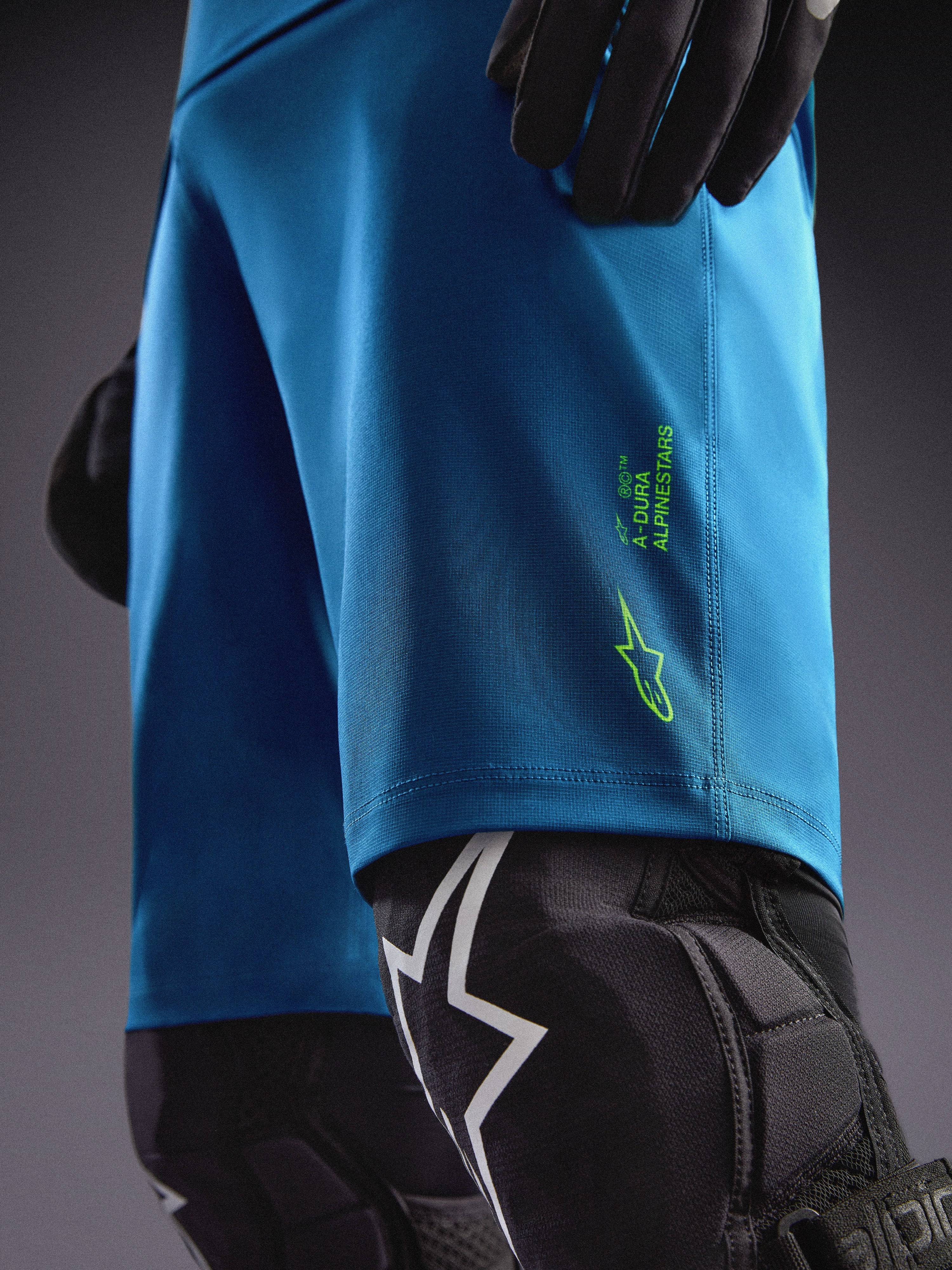 Alpinestars A-Dura Ride Shorts in Blaugrün mit limettengrünen Logos, kombiniert mit Knieprotektoren für MTB-Fahrten.