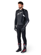 Männlicher Motorradfahrer in der Alpinestars Missile V3 Lederjacke in Schwarz und Weiß, mit einem weißen Brustlogo und perforierten Ledereinsätzen, kombiniert mit einer schwarzen Motorradhose, schwarzen Handschuhen und schwarz-roten Rennstiefeln für einen kompletten sportlichen Riding-Look.