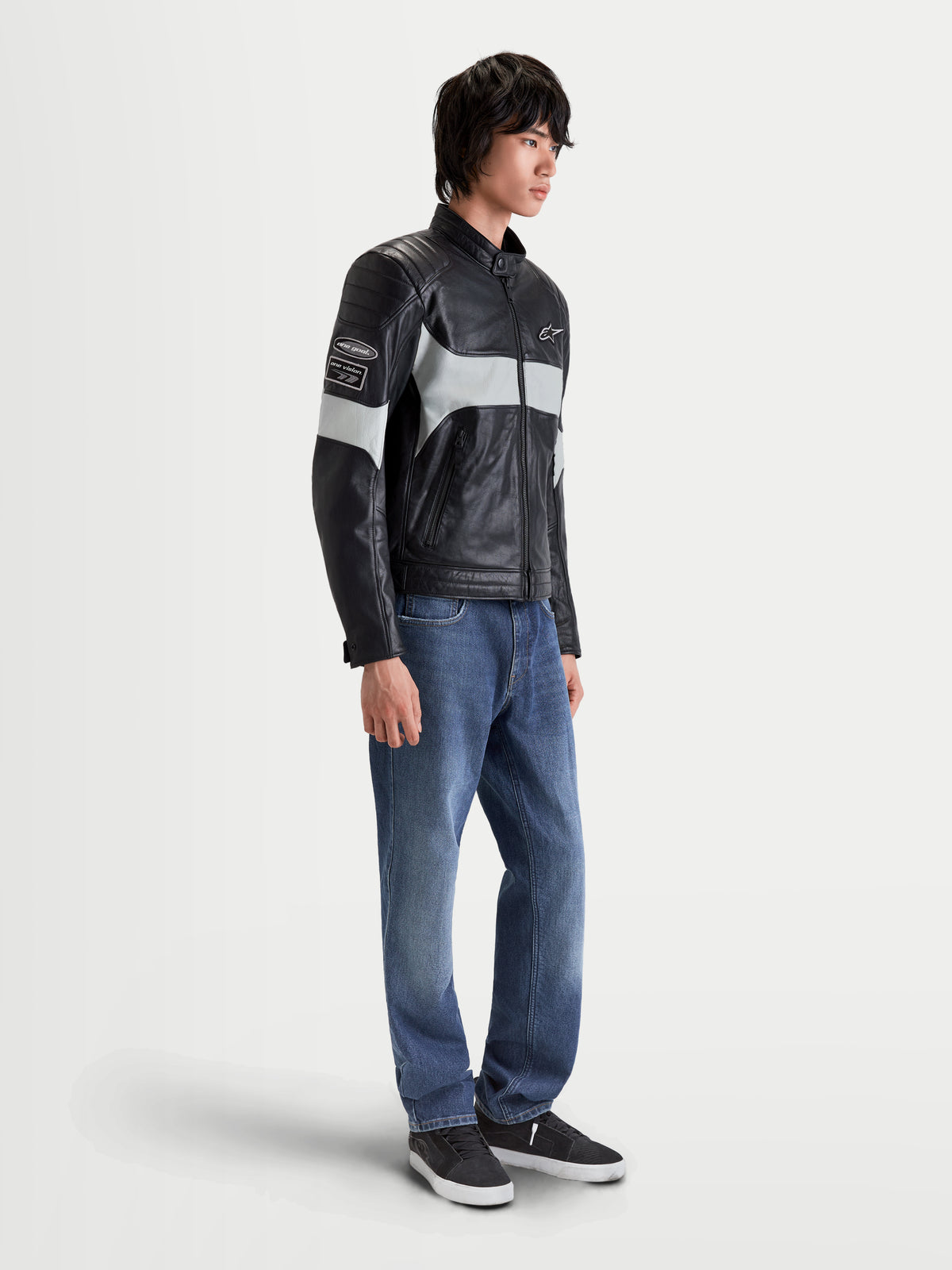 Alpinestars Revern Lederjacke, urbane Motorrad-Lederjacke für Herren in Schwarz und Metallgrau, Seitenprofil-Ansicht getragen von einem Model mit Jeans, mit genarbtem Vollnarbenleder und Heritage-Design