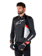 Alpinestars Missile V3 Airflow Lederjacke, Schwarz, Weiß und Fluo-Rot, Rennsport-Motorradjacke, getragen von einem Model mit passenden Handschuhen, mit perforierten Lederpanels, großem weißen Brust-Logo und schwarzen Schulterschleifern.
