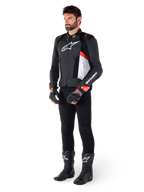 Alpinestars Missile V3 Airflow Lederjacke, Schwarz Weiß Rot Fluo, getragen von einem männlichen Model mit schwarzer Hose, schwarzen Rennhandschuhen und schwarzen Stiefeln, mit perforiertem Leder für Belüftung, weißem Brustlogo und fluoreszierenden roten Akzenten, entwickelt für erstklassige Renn- und Sport-Performance.