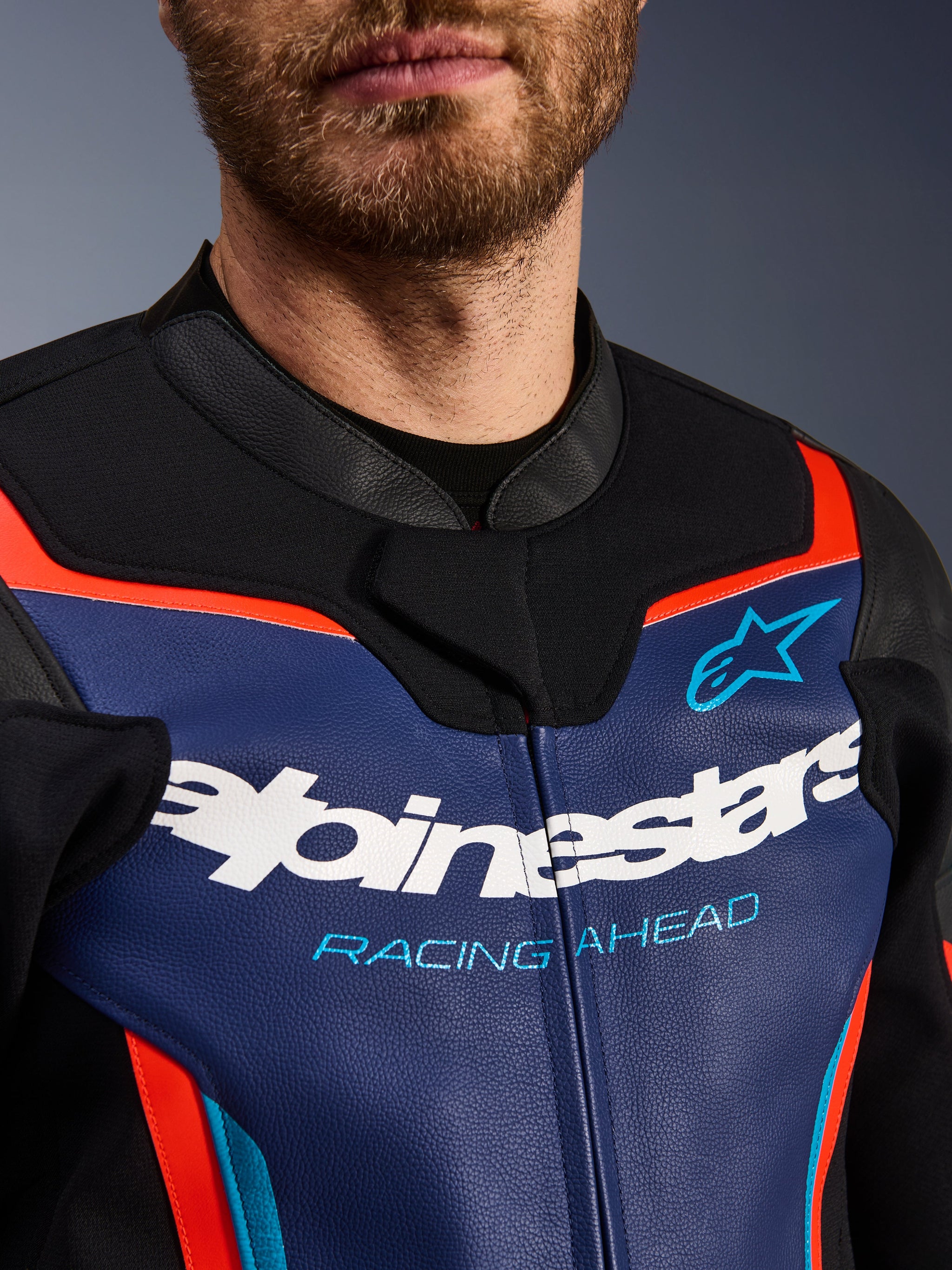 Alpinestars GP Force V2 Lederjacke, Detailansicht von Brust und Kragen, Blau, Schwarz und Rot Fluo, mit weißem Alpinestars-Logo und hellblauem 'RACING AHEAD'-Schriftzug, hochwertige Lederstruktur mit fluoreszierenden Akzenten