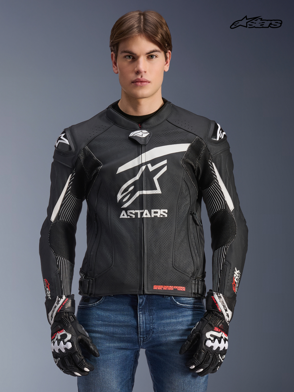 Alpinestars GP Plus R V4 Rideknit Lederjacke, Herren-Rennmotorradjacke in Schwarz und Weiß, Vorderansicht an einem Model mit passenden Handschuhen und Jeans, mit rennabgeleitetem Schutz und technischen Stretch-Paneelen