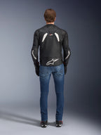 Rear view of the Alpinestars GP Plus R V4 Rideknit Leather Jacket, Black and White, featuring a large white logo on the lower back and branding on the sleeves, worn with blue riding jeans and black boots, highlighting the technical construction and sport fit.