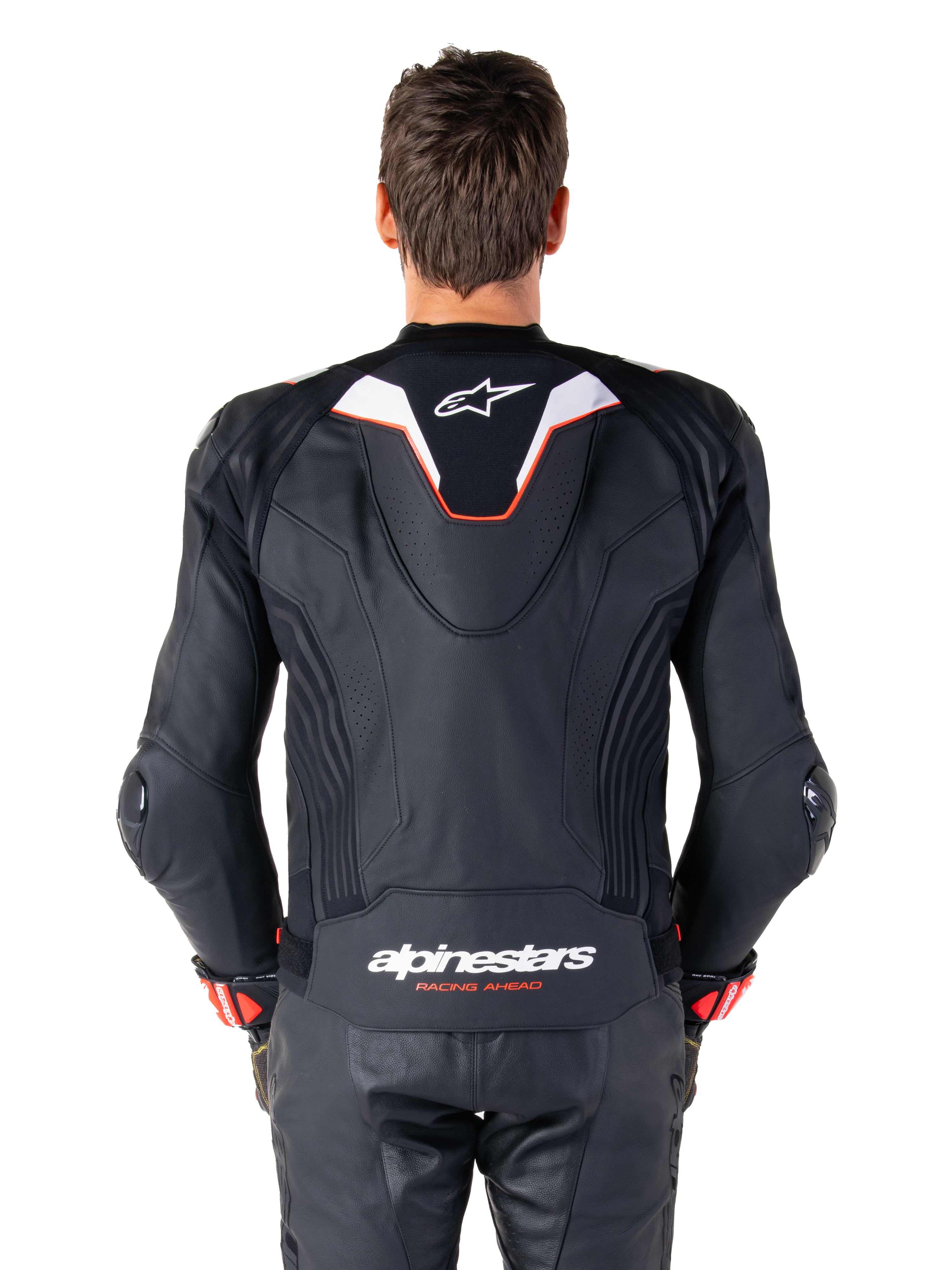 Rear view of a rider wearing the Alpinestars Missile V3 Ignition Leather Jacket, black leather with white and red accents, featuring a slim sport aero-hump with a white logo and 'alpinestars RACING AHEAD' branding on the lower back, paired with matching black leather racing pants and gloves.