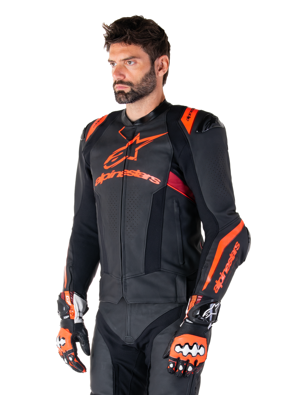 Alpinestars Missile V3 Ignition Lederjacke, Schwarz mit Akzenten in Red Fluo und Dark Red, getragen von einem männlichen Model mit passenden Rennhandschuhen und Lederhose, mit auffälligem Alpinestars-Branding, perforierten Ledereinsätzen und externen Schulterprotektoren, professionelle Motorrad-Rennausrüstung