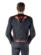 Alpinestars Missile V3 Ignition Lederjacke, Rückansicht, Schwarz mit Akzenten in Red Fluo und Dark Red, mit sportlichem Aero-Höcker, Alpinestars-Branding auf dem Rücken, getragen mit passender schwarzer Leder-Motorradhose, Performance-Motorrad-Rennausrüstung