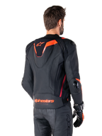 Alpinestars Missile V3 Ignition Lederjacke, Herren-Rennsportjacke, Schwarz mit Red Fluo Akzenten, Rückansicht mit schmalem aerodynamischem Sport-Höcker und Alpinestars-Logo am unteren Rücken, getragen mit schwarzer Lederhose und Rennsport-Handschuhen, schlankes professionelles Motorsport-Design