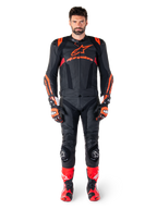 Männliches Model in der Alpinestars Missile V3 Ignition Lederjacke in Schwarz, Fluo-Rot und Dunkelrot, komplette Motorrad-Rennausrüstung mit passender Lederhose, Rennhandschuhen und Stiefeln, markantes Alpinestars-Branding auf der Brust, nach vorne gerichtete Pose, professionelles Sport-Fahrer-Outfit