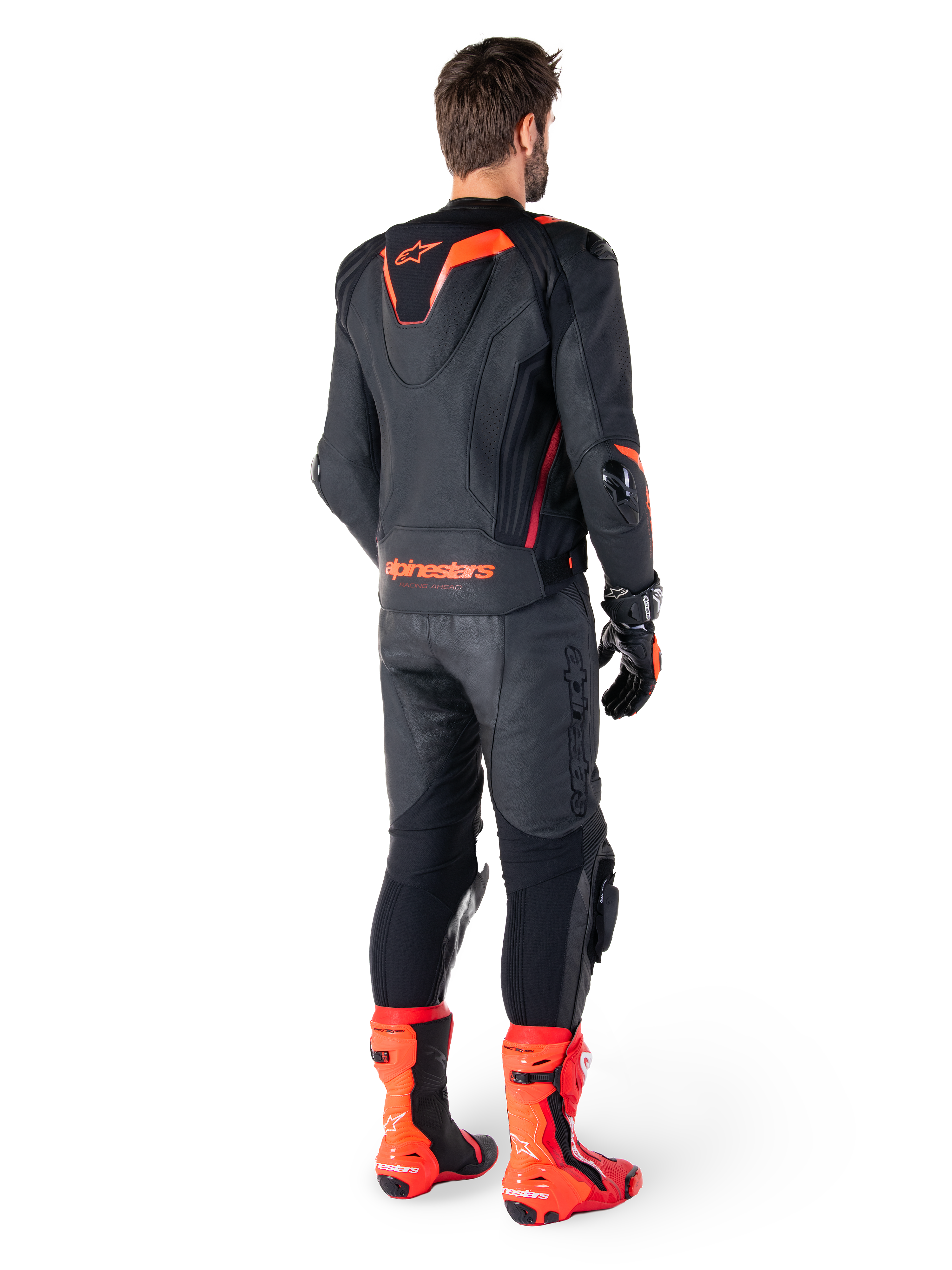 Alpinestars Missile V3 Ignition Lederjacke, Rennsport-Motorradjacke, Schwarz und Rot Fluo, Rückansicht eines Fahrers in vollständiger Rennbekleidung mit passender Lederhose, Handschuhen und roten Stiefeln, mit sportlichem Aero-Höcker und markantem Branding am unteren Rücken.