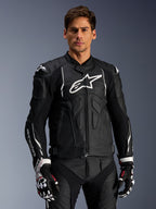 Alpinestars Dusk Lederjacke, Schwarz und Weiß, Motorrad-Lederjacke mit gepolsterten Schutzbereichen und weißen Logos, getragen mit schwarz-weißen Rennhandschuhen mit roten Akzenten, professionelle Sport-Fahrausrüstung